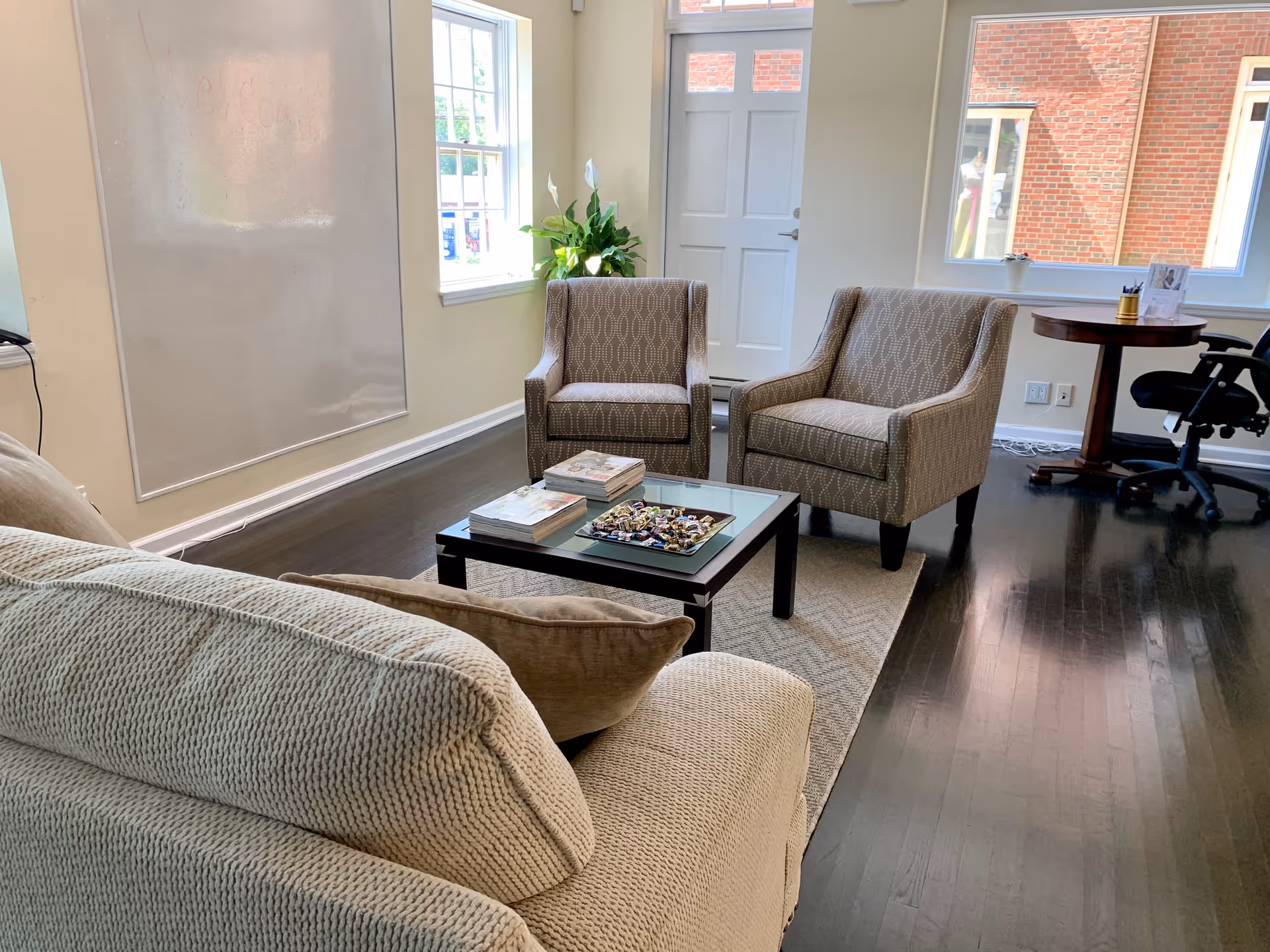Living room-style seating area with beige couches, two chairs, coffee table, magazines, and a desk.
