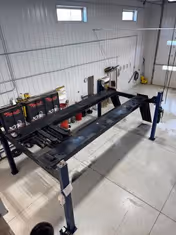 Inside a maintenance bay with a vehicle lift, tools, and shelves.