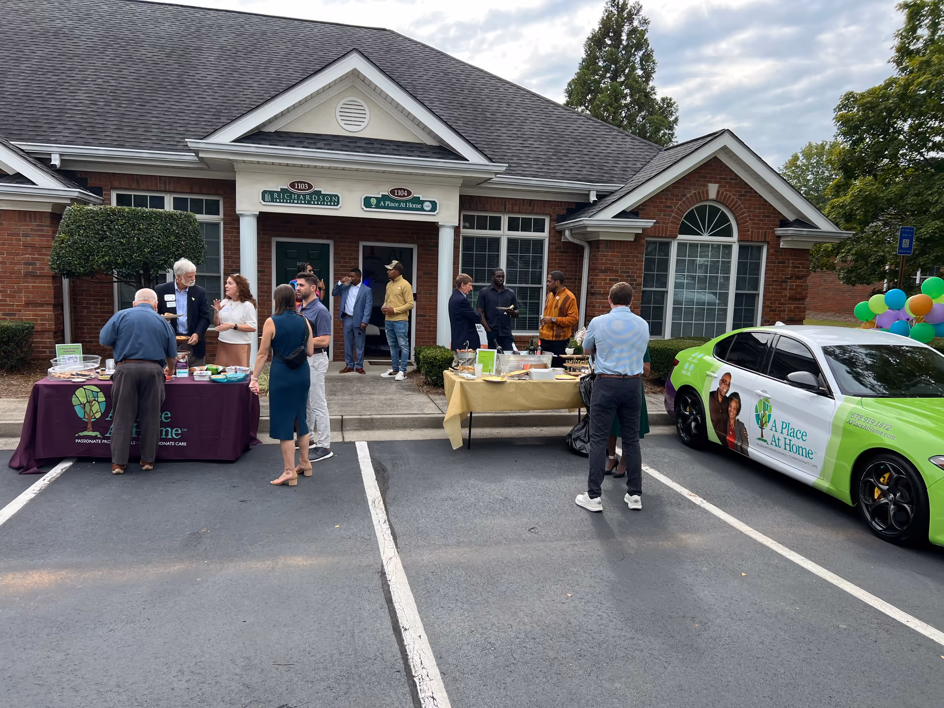 Outdoor parking lot event in front of A Place At Home Alpharetta with tables and people.