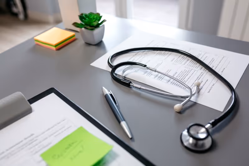 Desk layout with stethoscope, documents, pen, sticky notes, and a small plant.