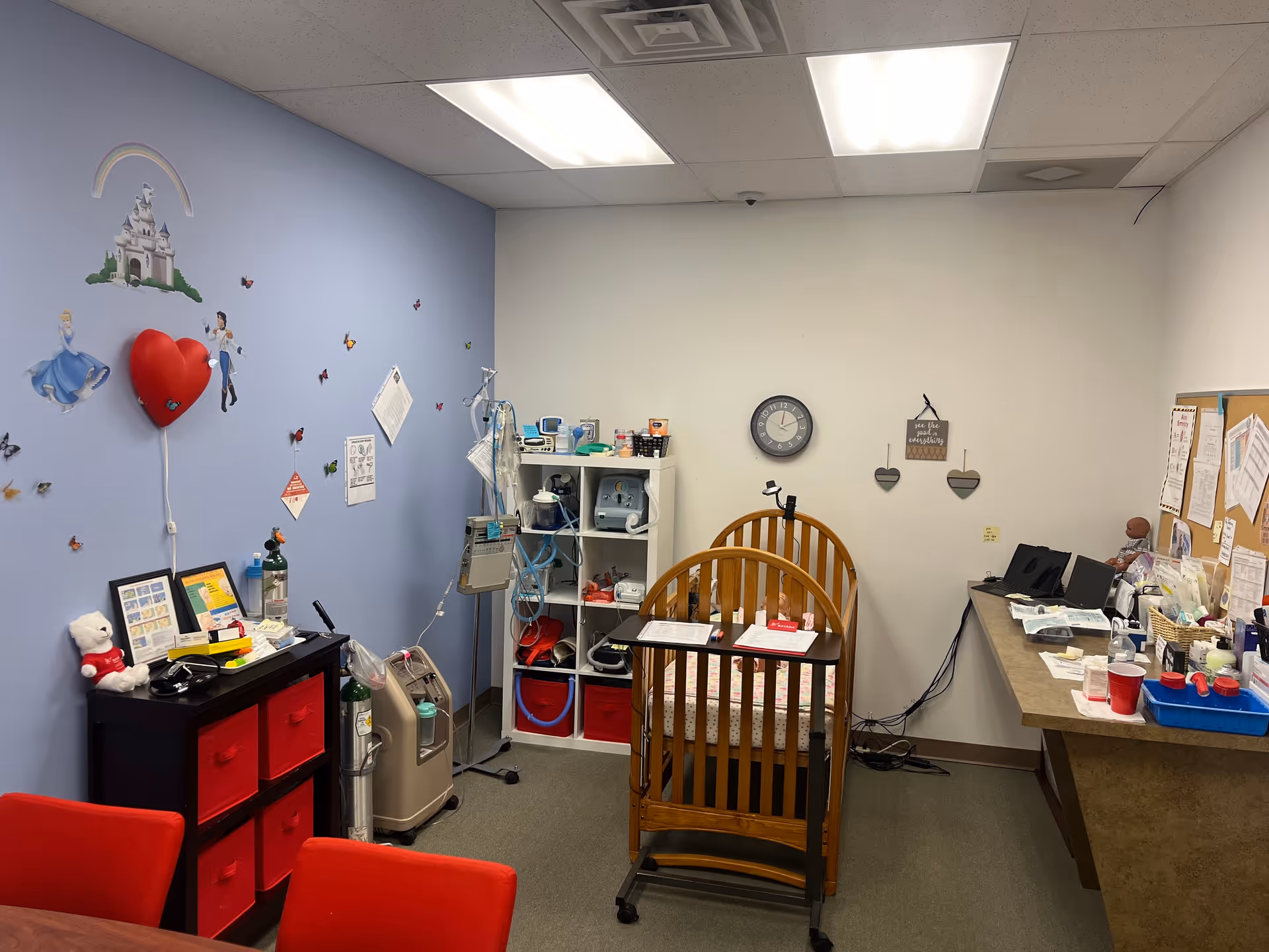 A pediatric care room with a wooden crib, medical equipment, and a desk.