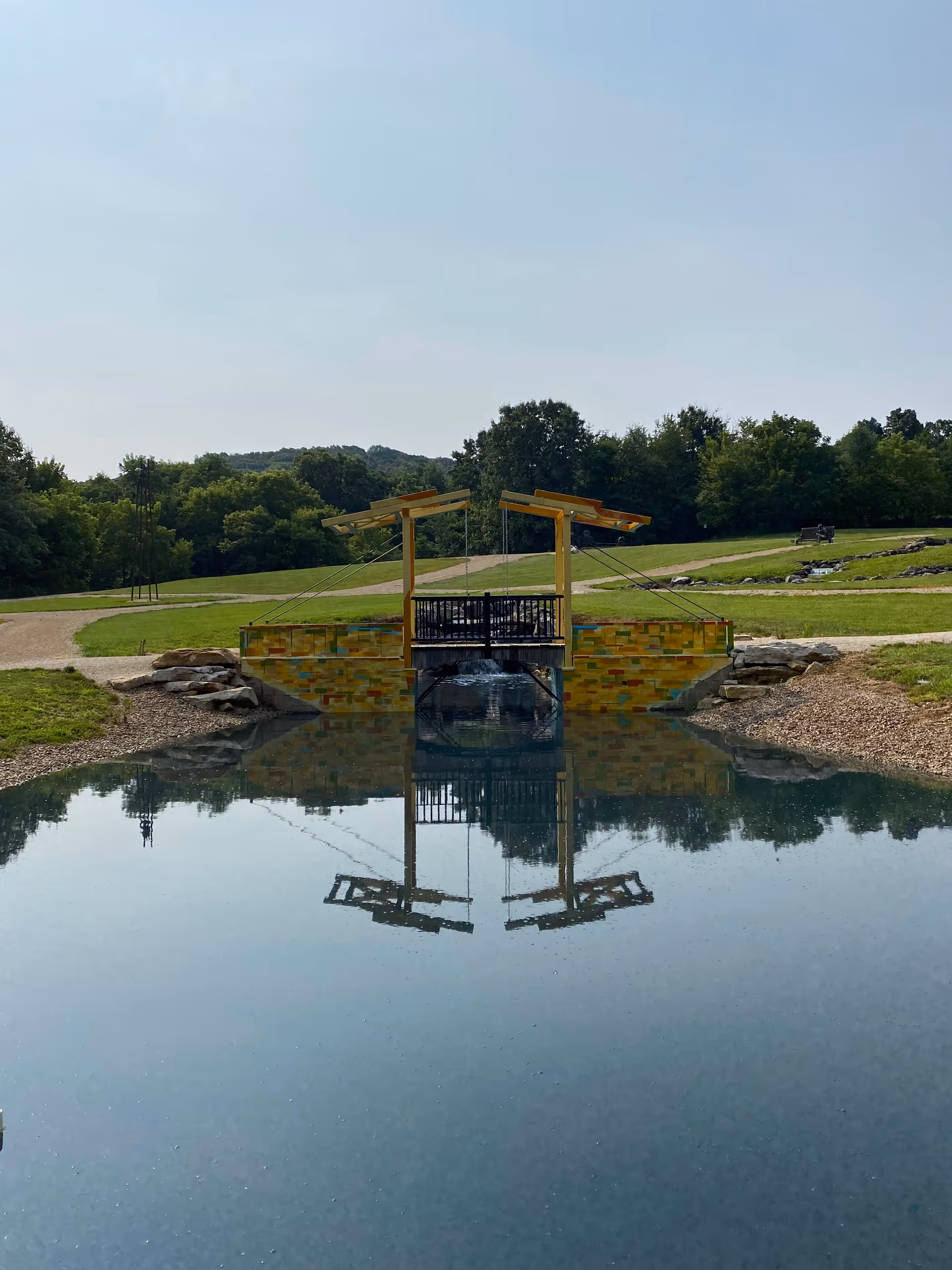 A small decorative wooden bridge over a calm pond with green landscaping.