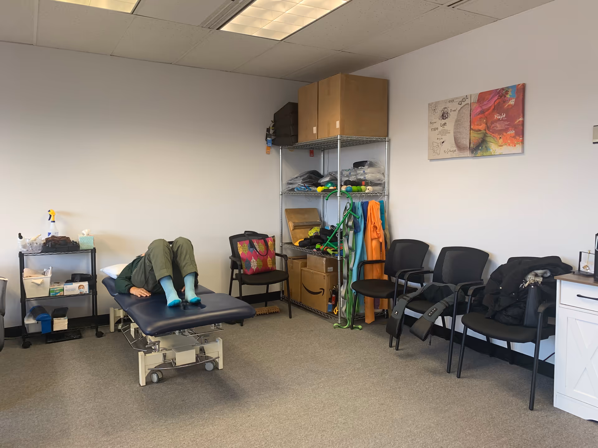 Patient lies on a treatment table in a therapy room with shelving and chairs.