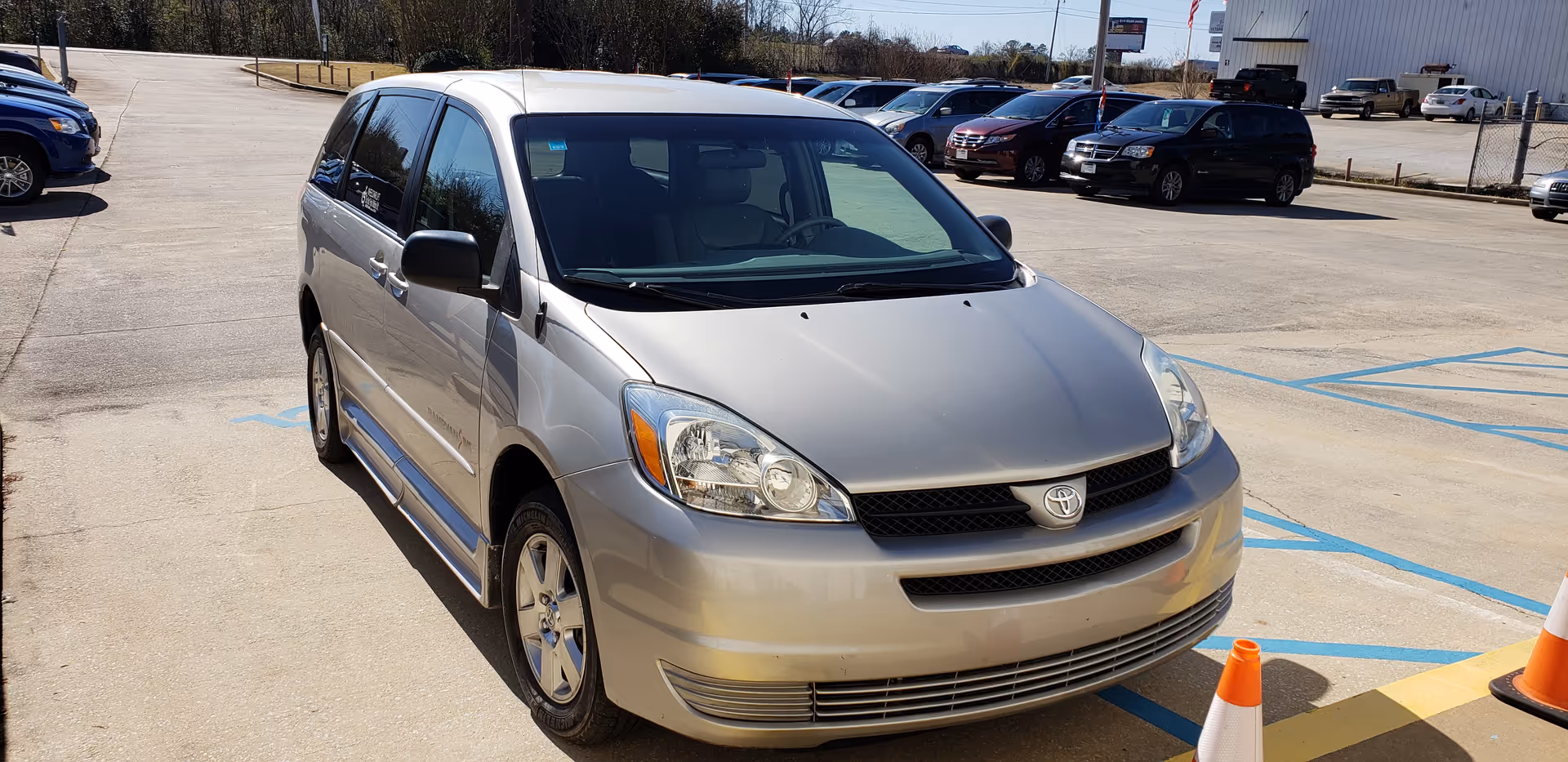 Silver Toyota minivan parked in a large lot with blue handicap markings and orange cones.