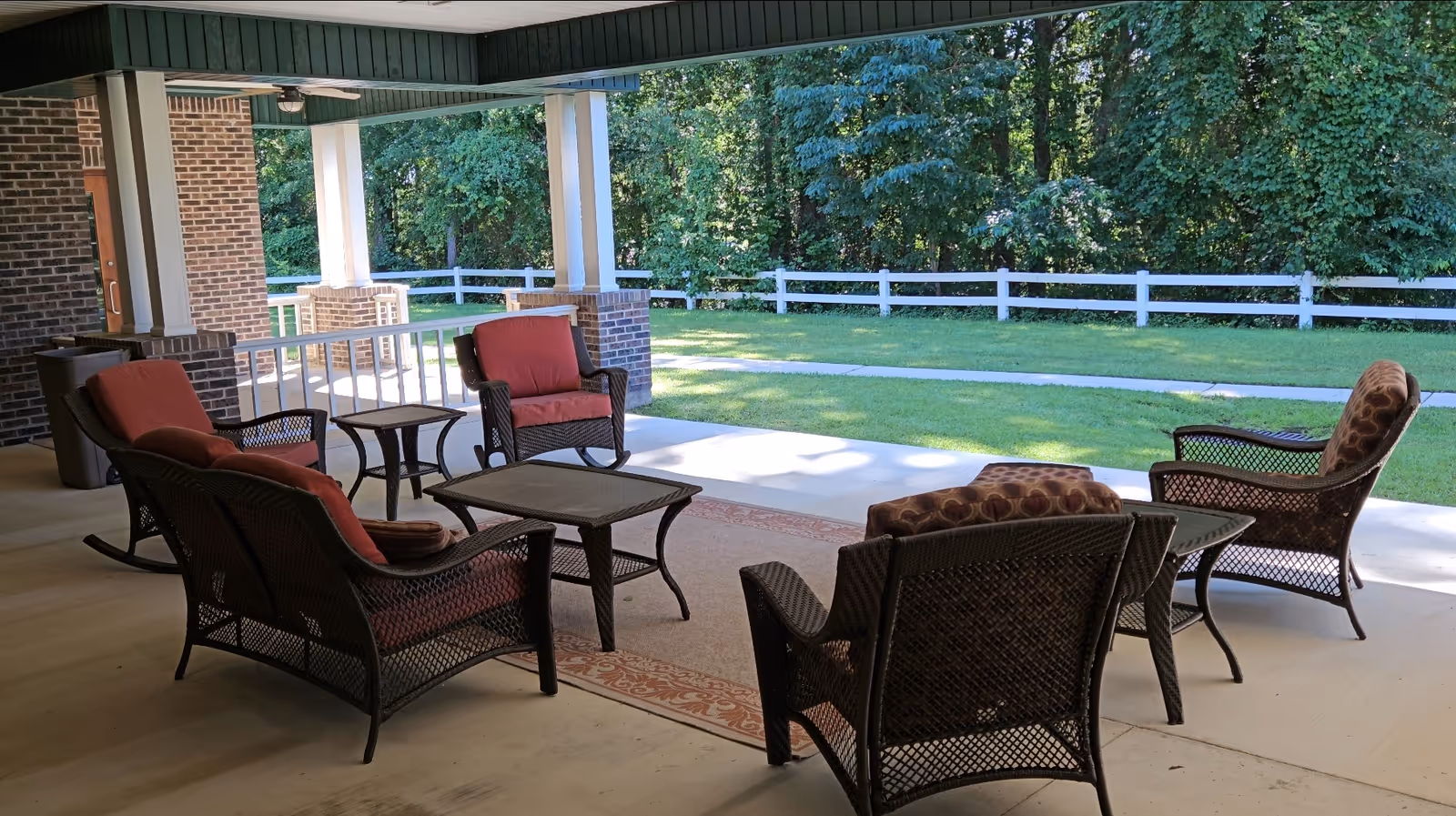 Shaded outdoor covered patio with wicker seating and tables.