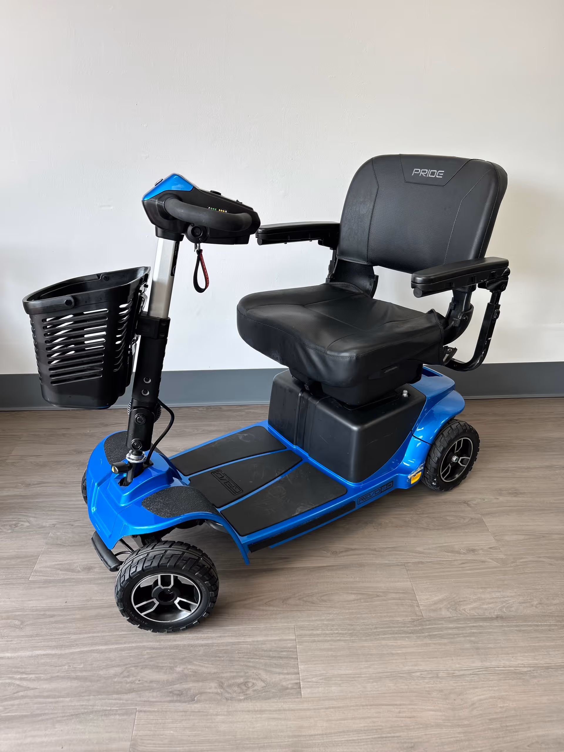 Blue mobility scooter with front basket indoors on wood-like flooring.