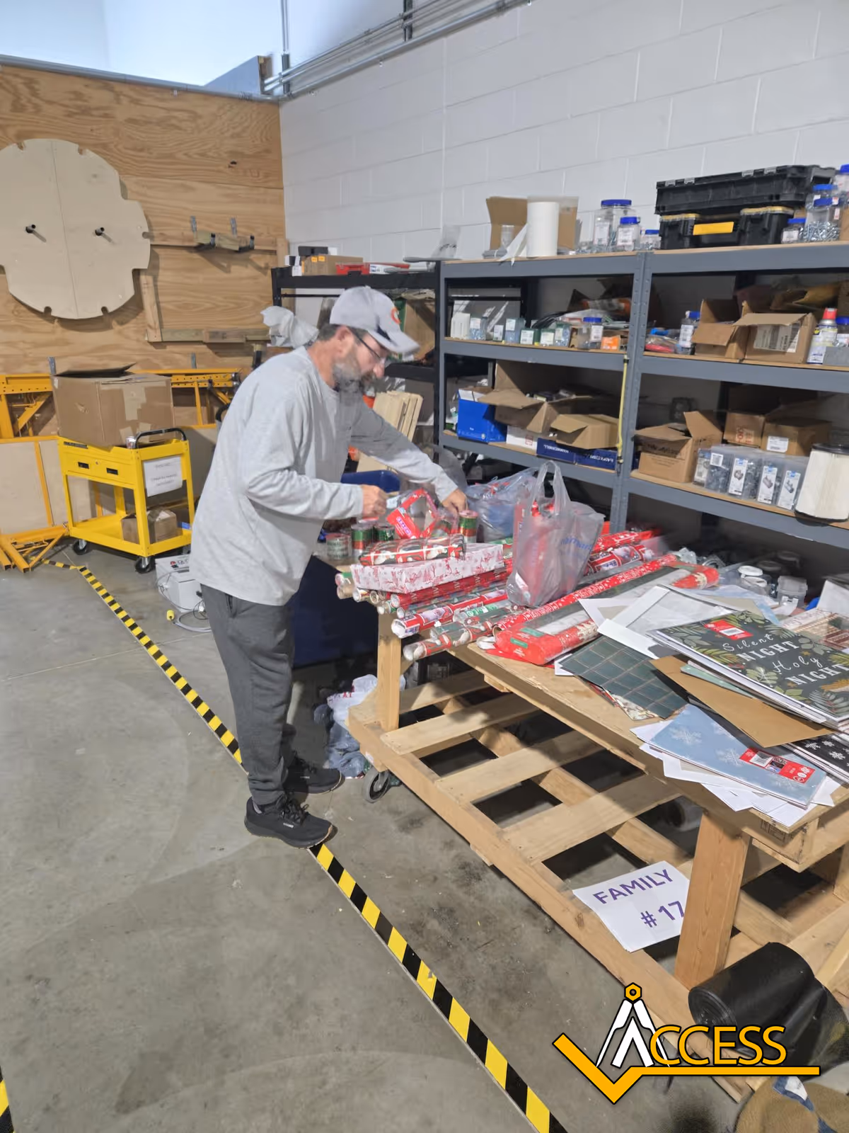 Man in gray shirt and cap organizing supplies on a cluttered workshop table.