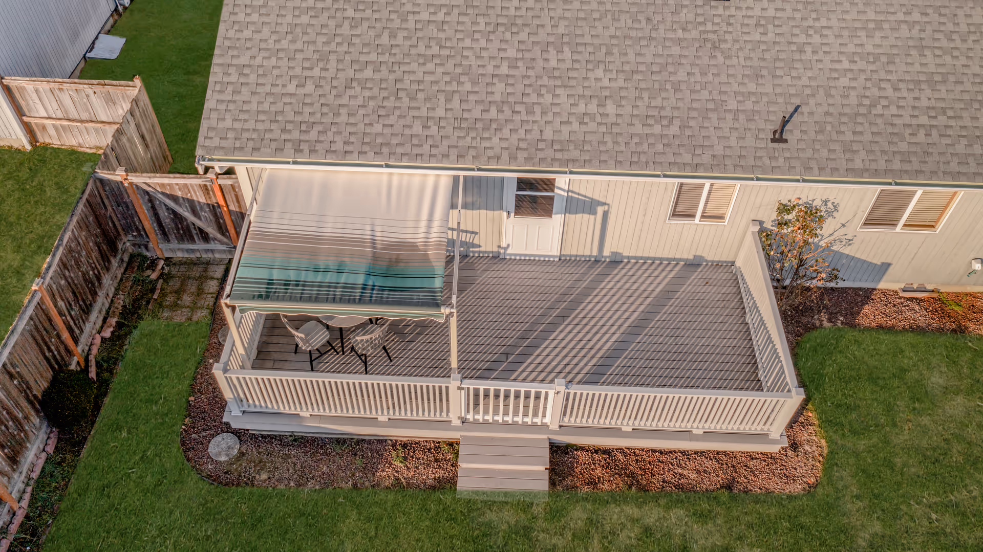 A wooden deck with railing attached to a single-story home, outdoor seating under an awning.
