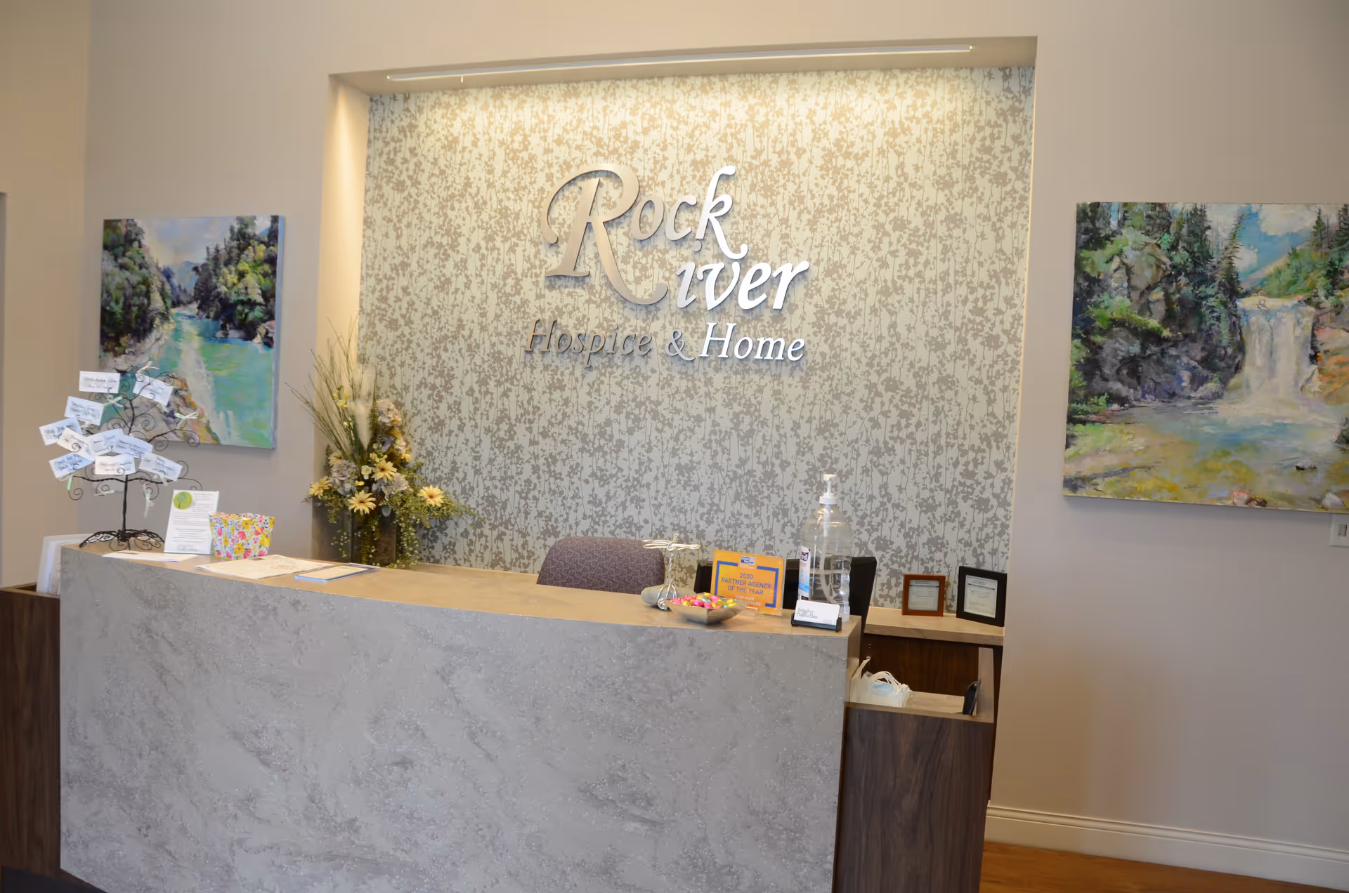 Reception desk in a Rock River Hospice & Home interior featuring a patterned wall and logo.