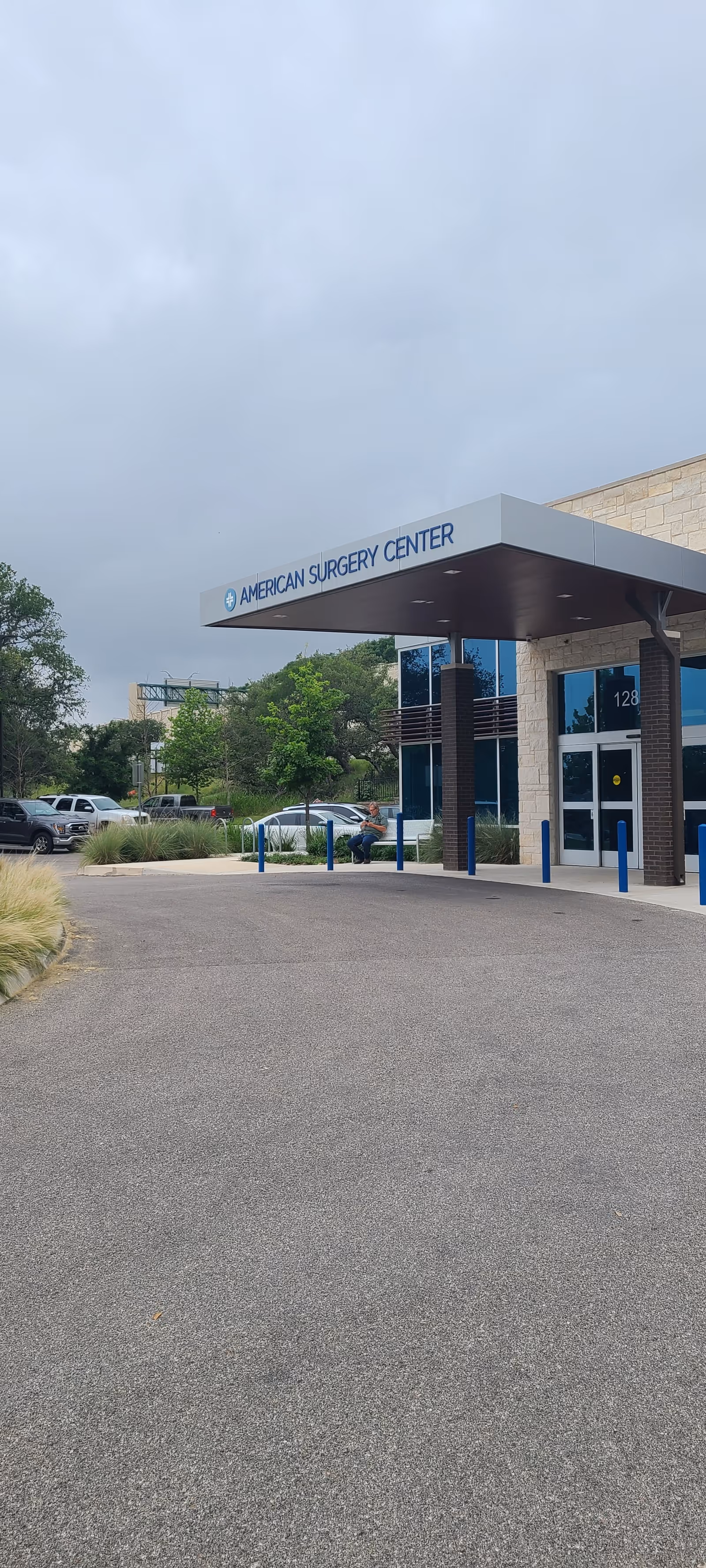 Exterior view of American Surgery Center entrance with canopy, cars, and landscaping.