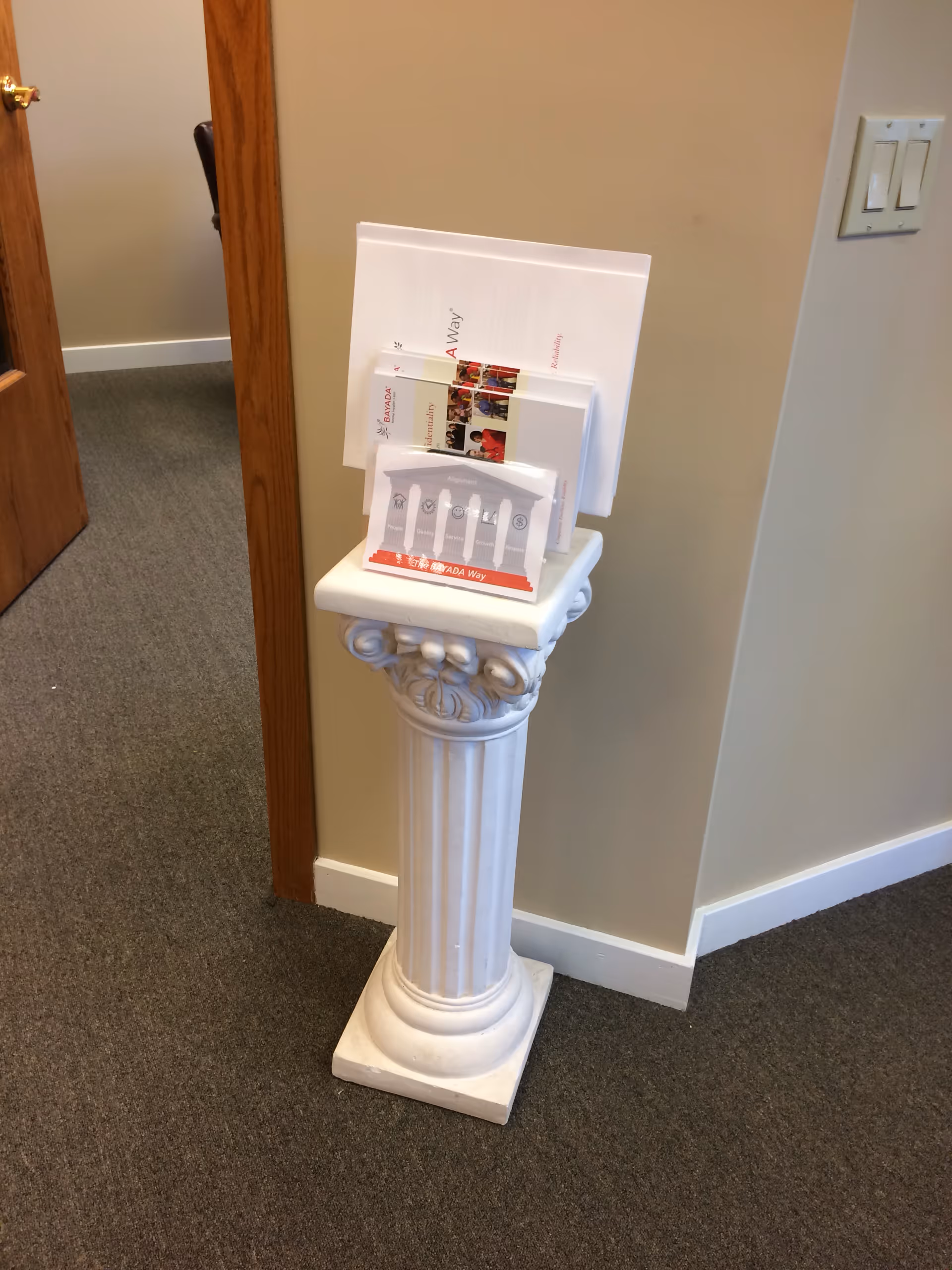 Indoor hallway with a white decorative pedestal holding brochures in front of a beige wall.
