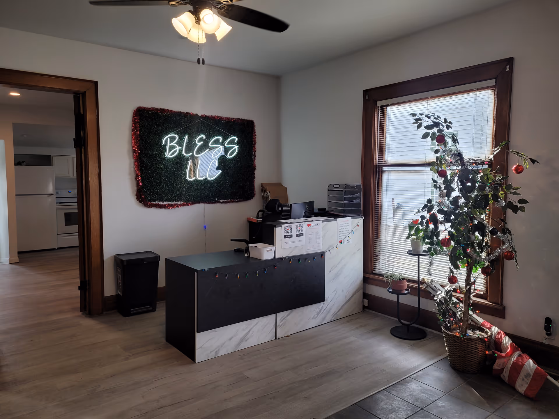 Reception counter inside a facility with a neon Bless LLC sign and a potted tree.