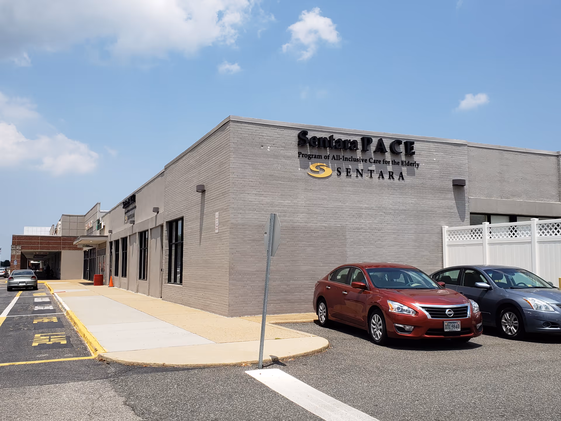Exterior view of the Sentara PACE facility with a parking lot and several cars.