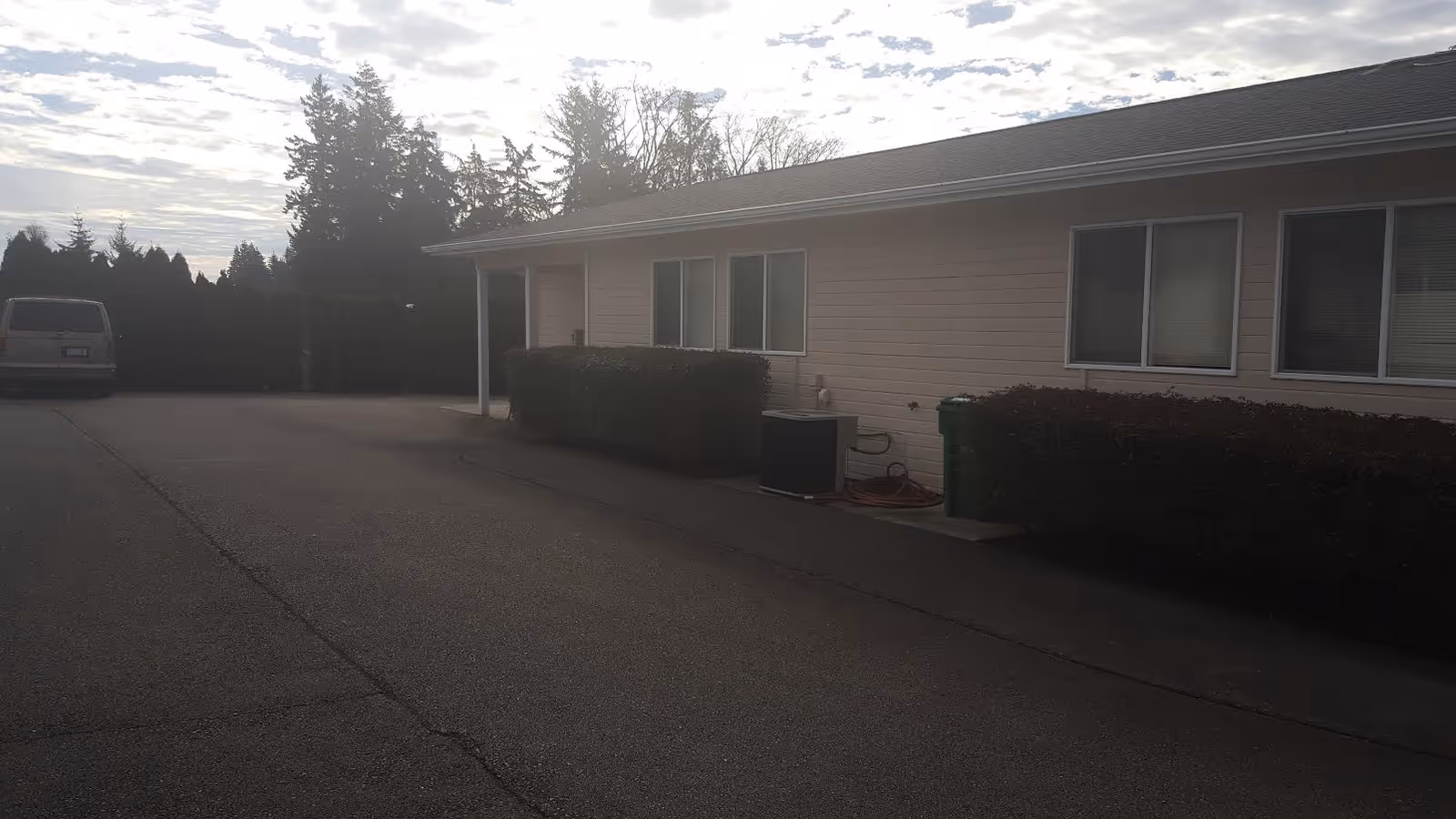 Single-story senior living facility exterior with windows, hedges, and a paved driveway.