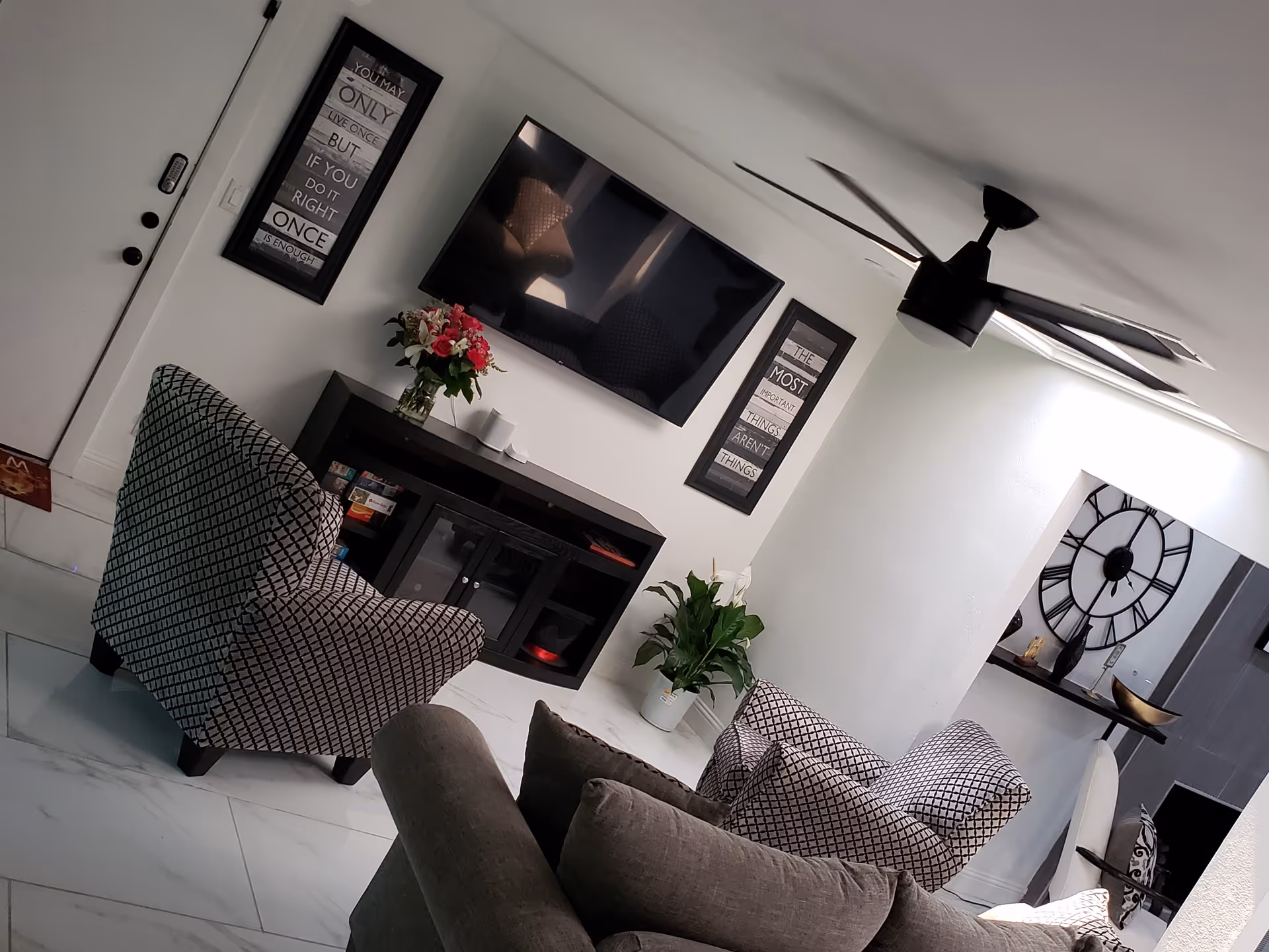 Modern living room in a senior facility with TV, chairs, plants, and wall art.