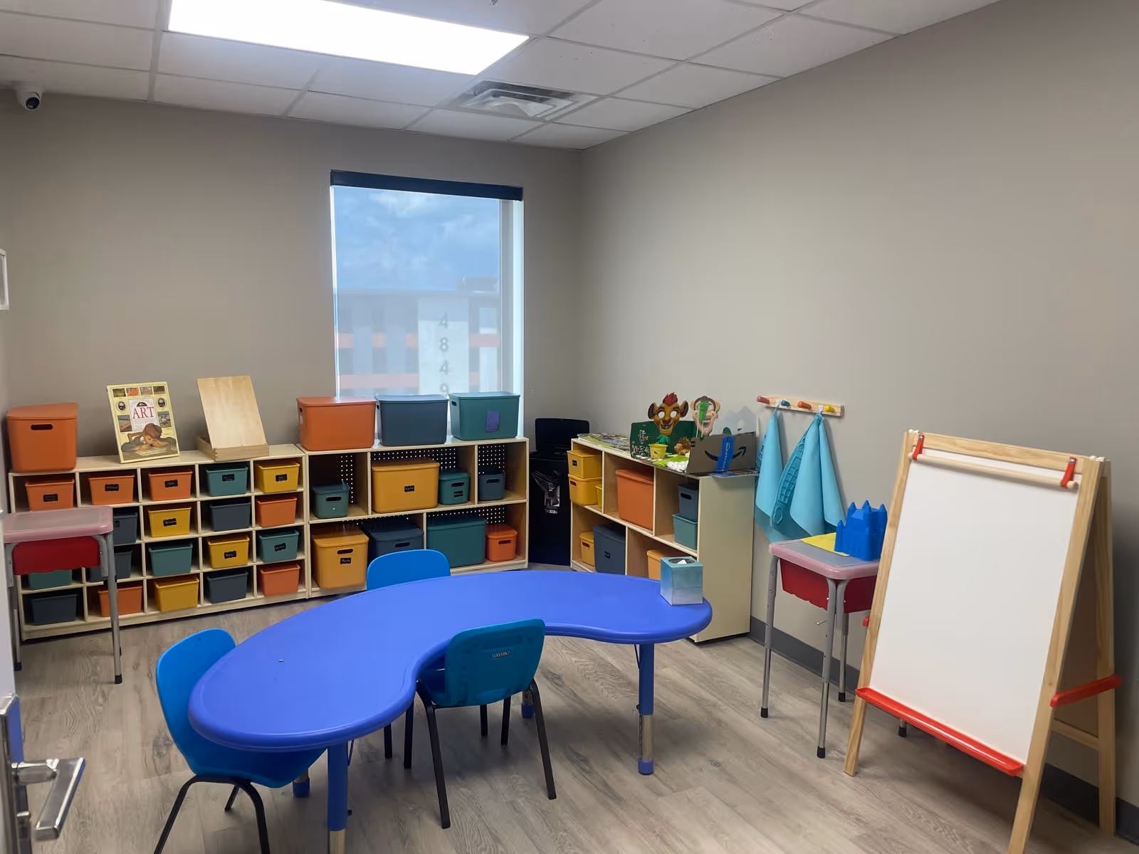Colorful activity room with cubbies, tables, an easel, and storage bins.