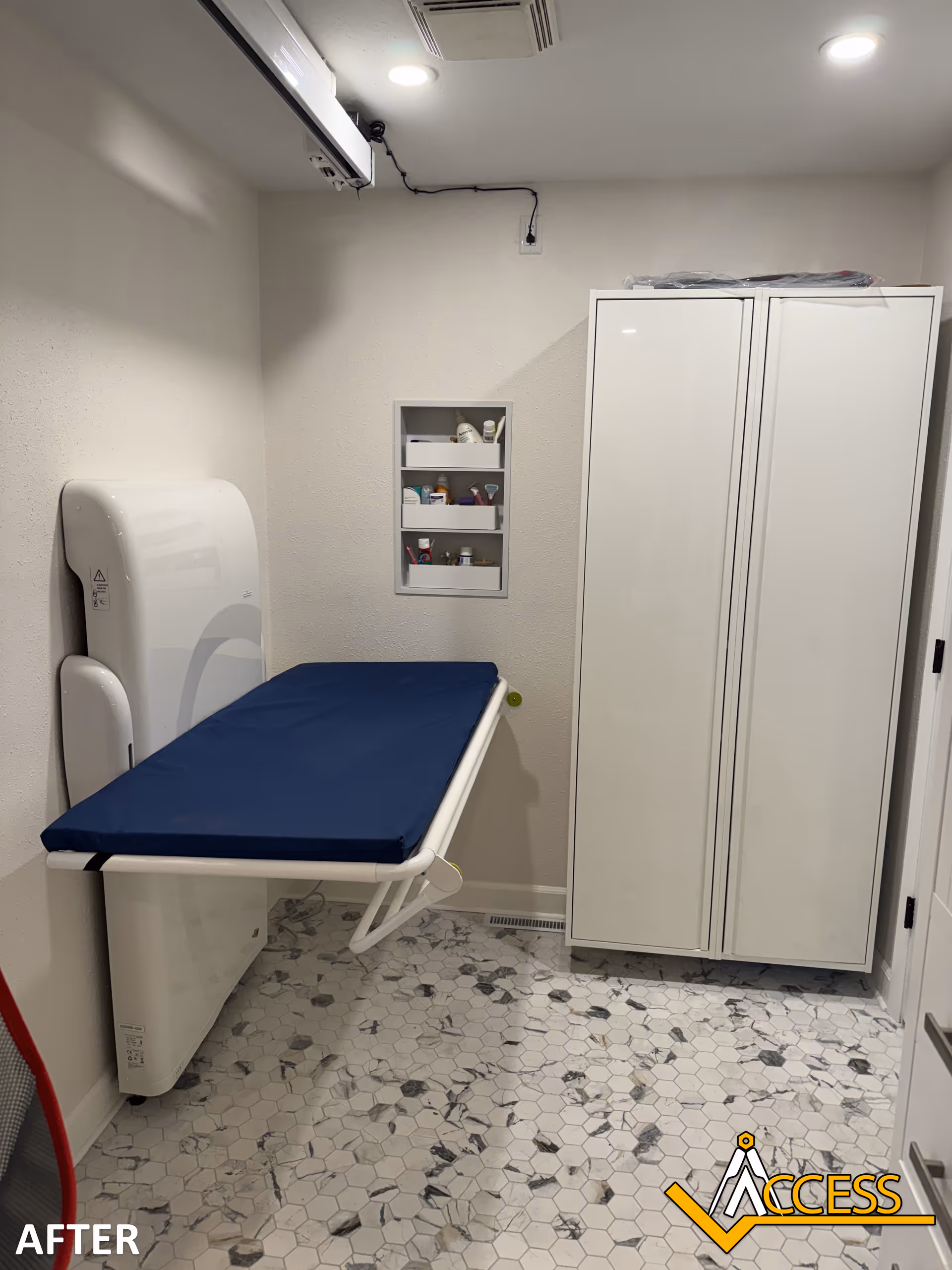 Small medical exam room with a blue padded examination table and white cabinets.