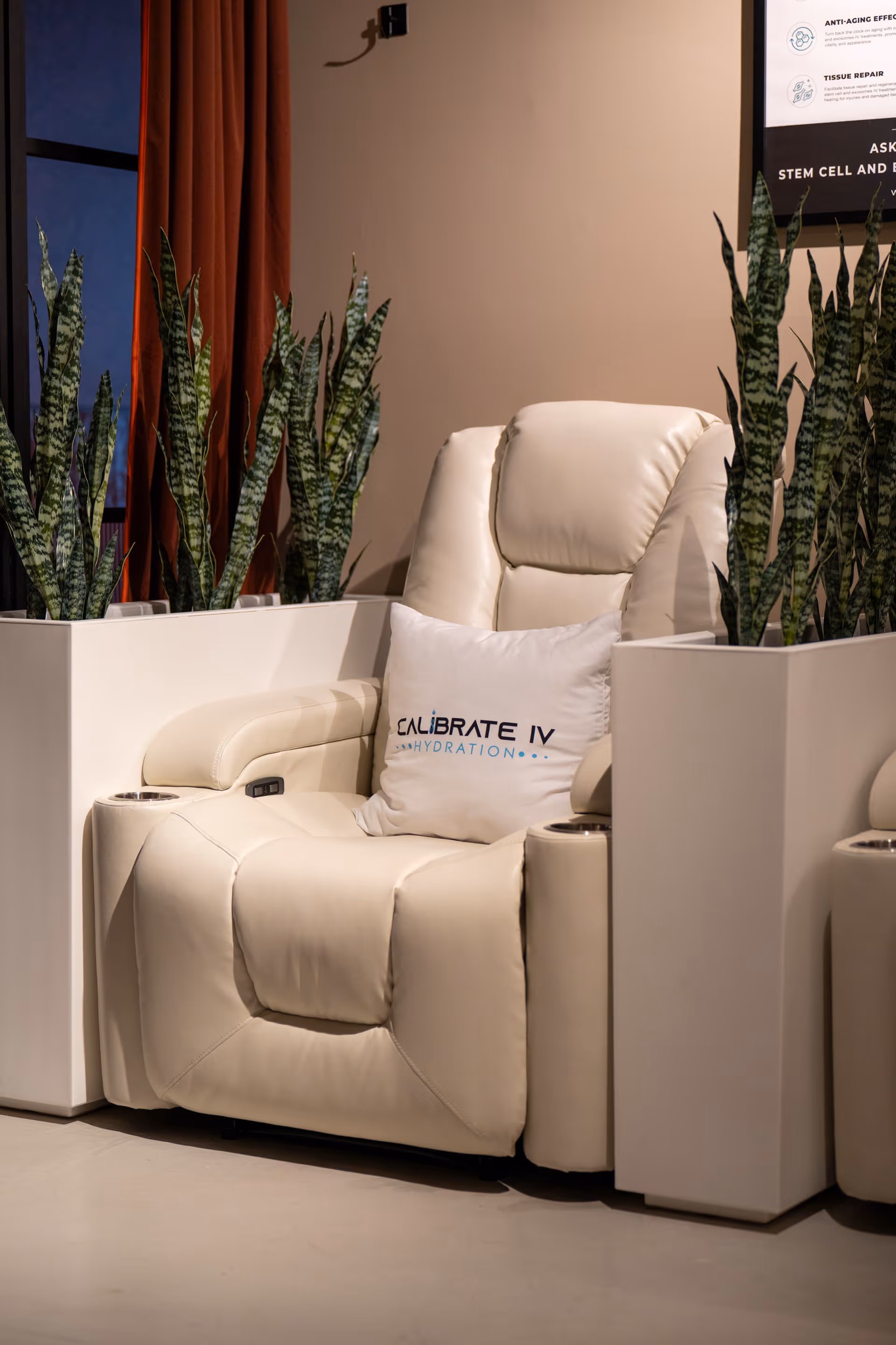 White leather lounge chair with Calibrate IV Hydration pillow beside tall planters.