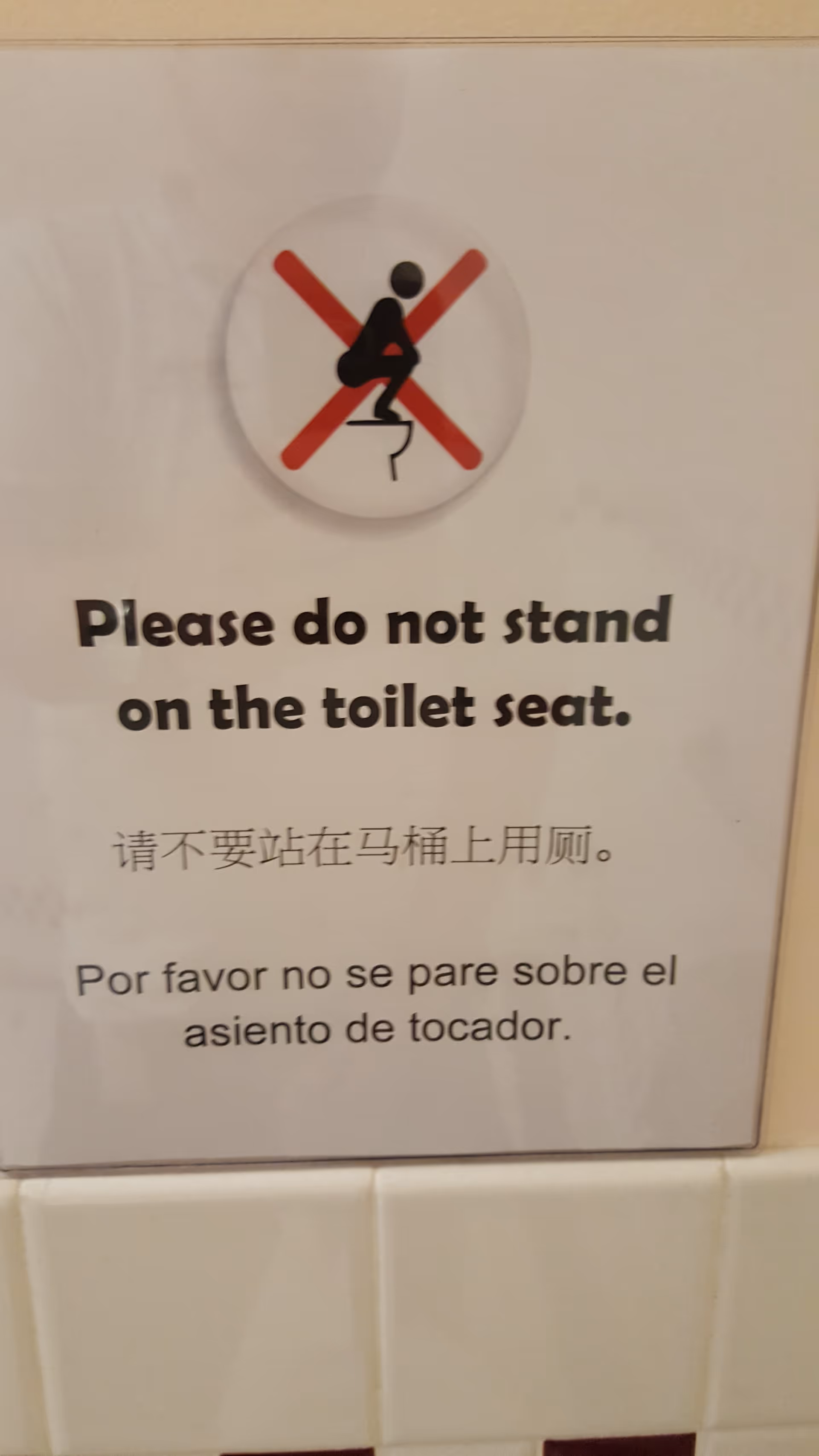 Sign on bathroom wall reading 'Please do not stand on the toilet seat' with translations.