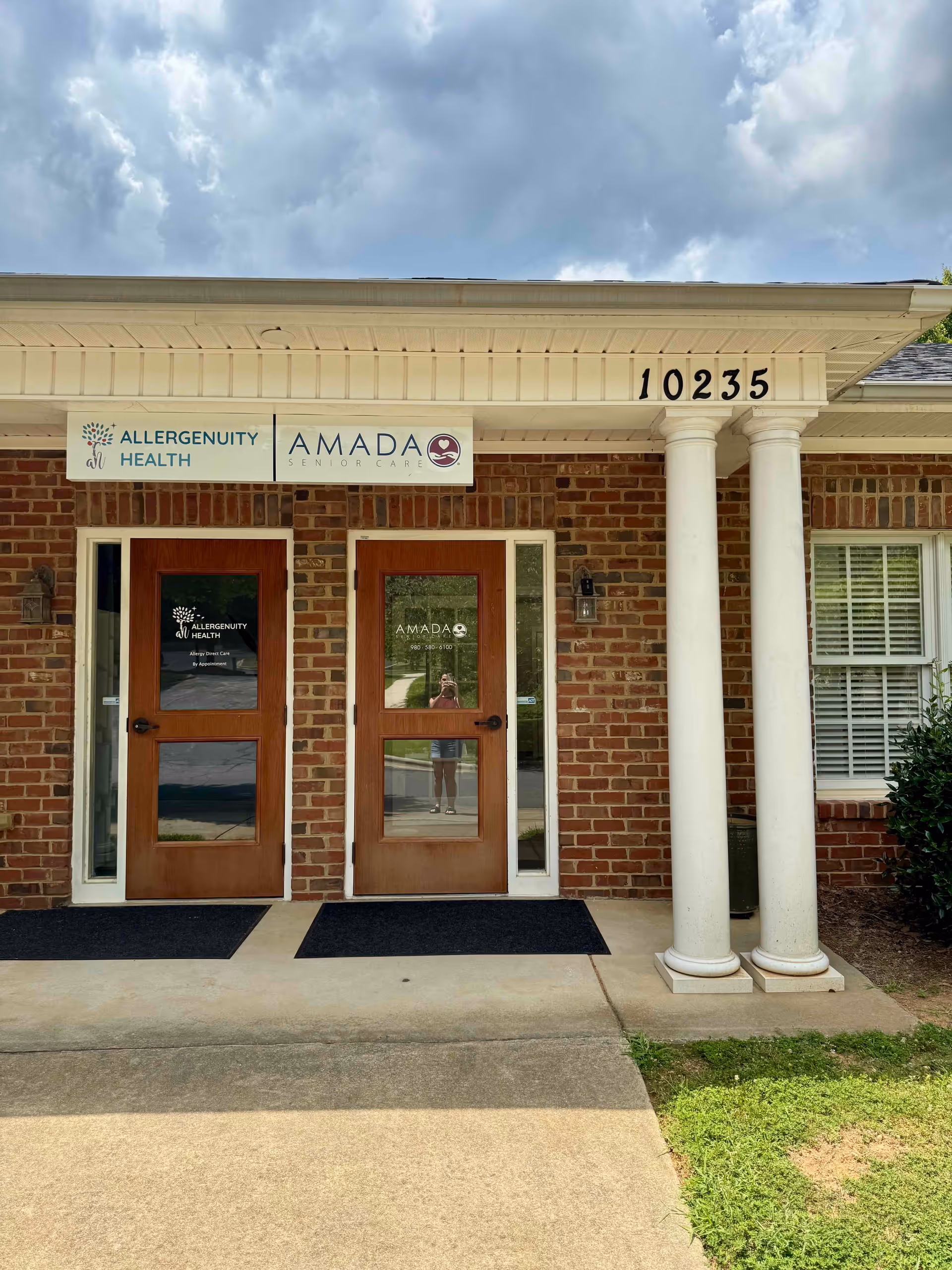 Front entrance of Amada Senior Care facility with brick exterior, double wooden doors, and columns.