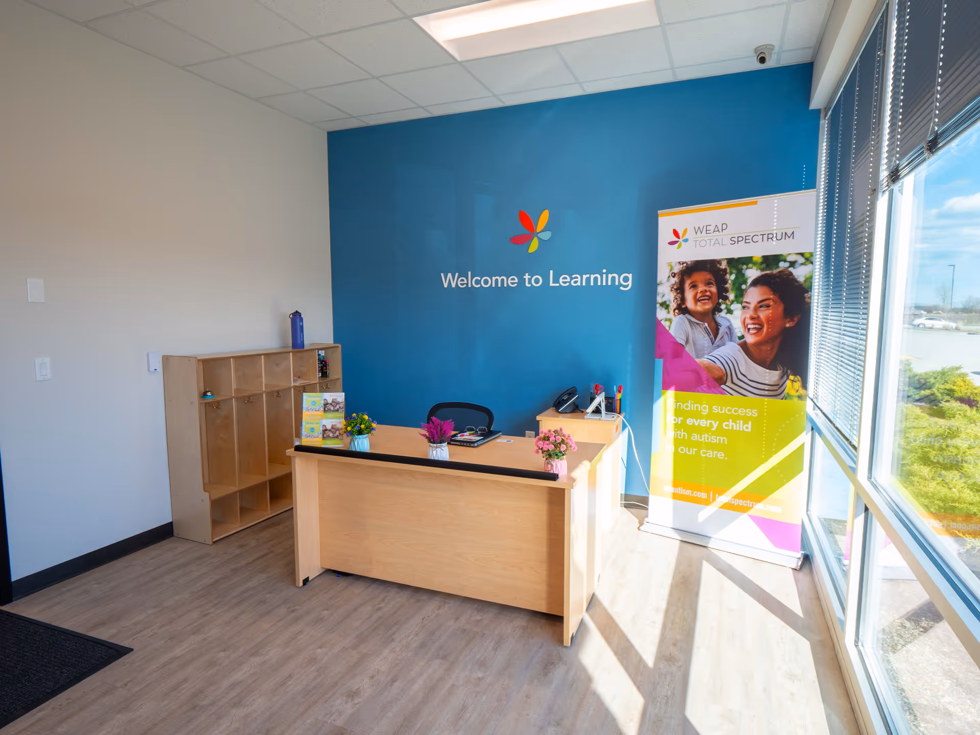 A reception desk sits inside a bright learning center with a blue wall and banner.