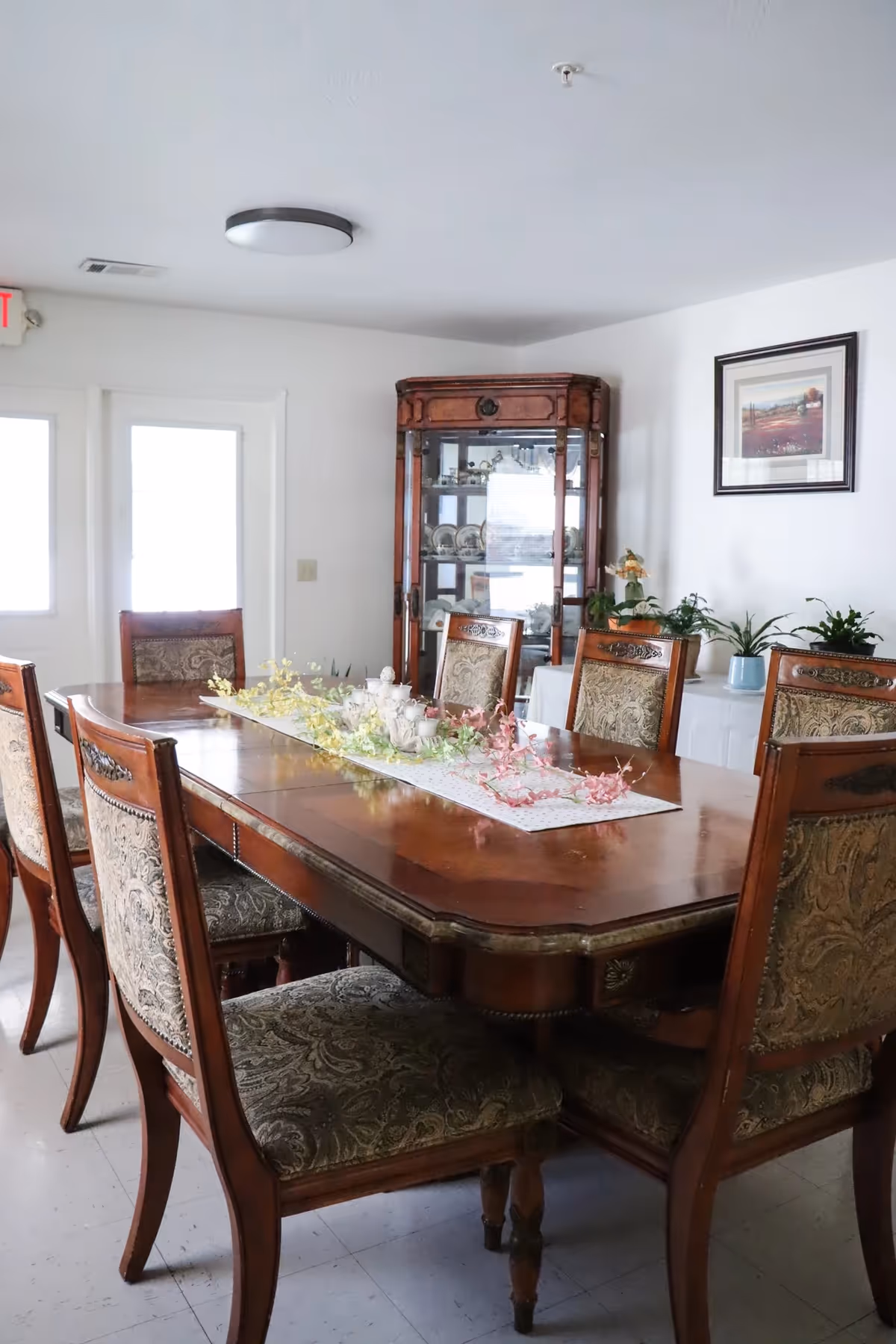 Classic dining room with a long wooden table, upholstered chairs, and a glass-front cabinet.