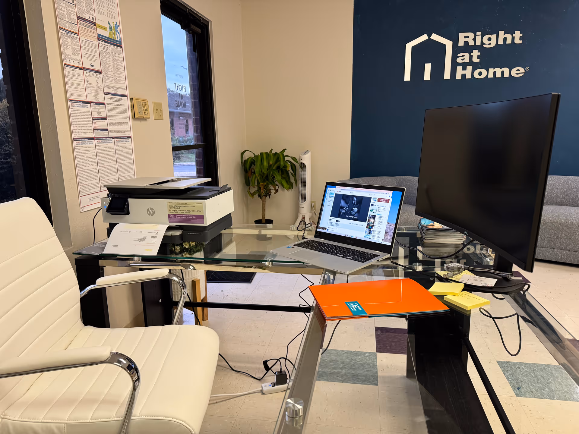 Office reception area with glass desk, laptop, printer, and Right at Home logo.