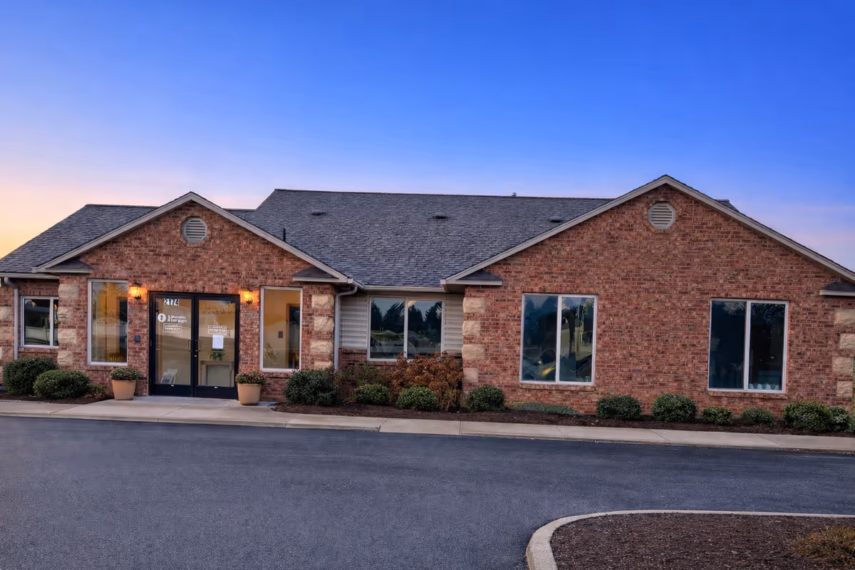 Brick senior living facility exterior with entrance doors and shrub-lined front.