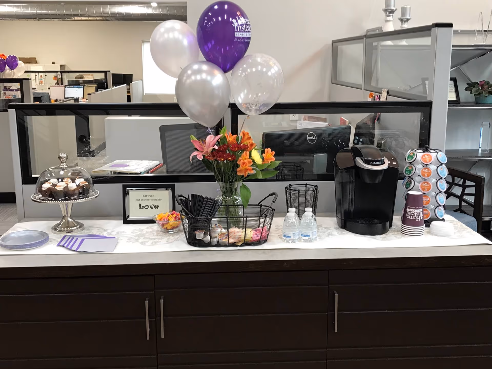 Reception counter with balloons, flowers, beverages and snacks inside a senior living facility.