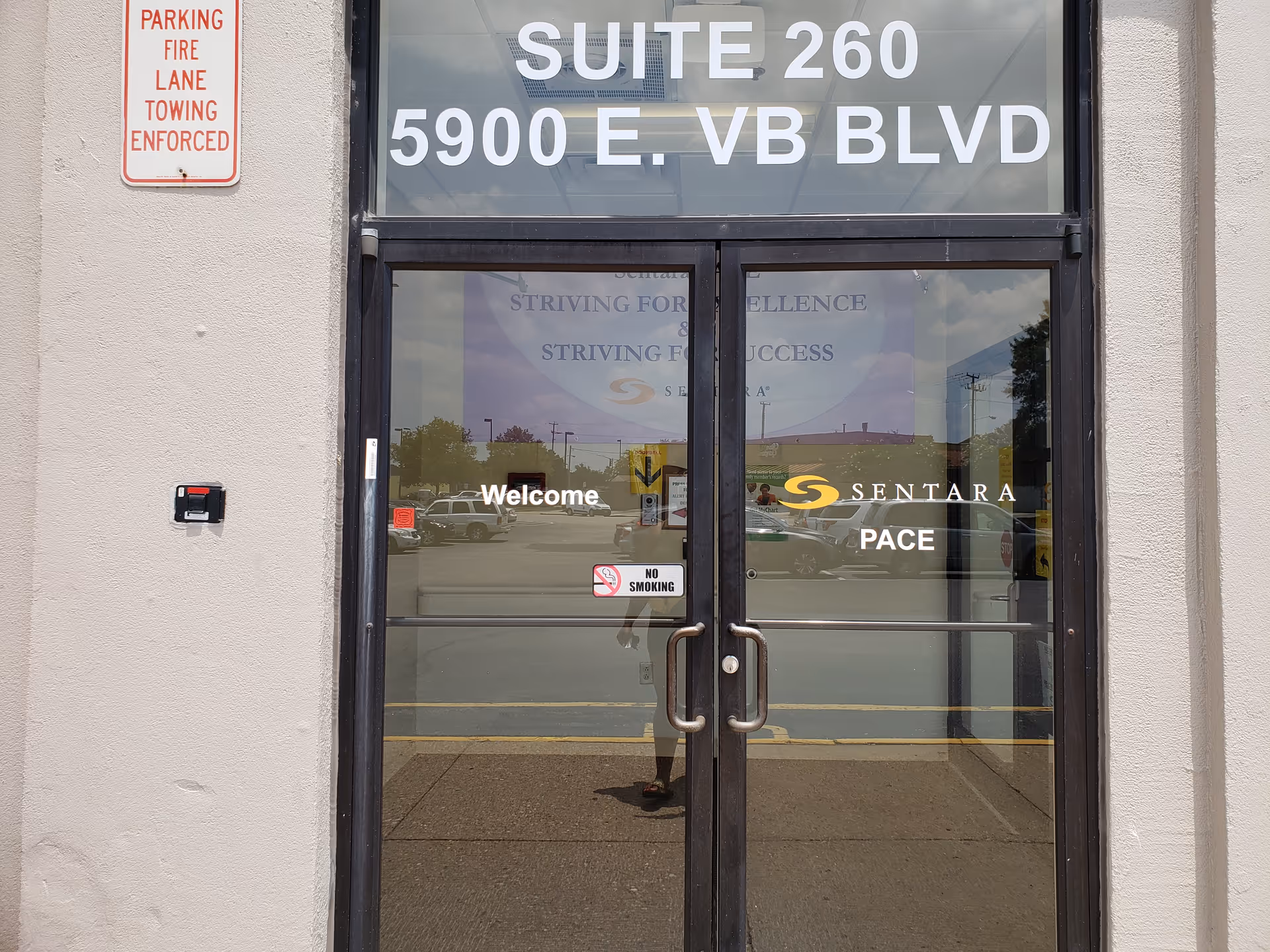 Glass double doors with a welcome sign and Sentara PACE branding are at the building front.