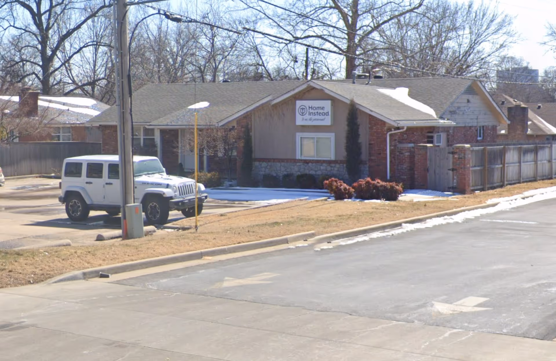 Single-story Home Instead building along a street with a white SUV parked.
