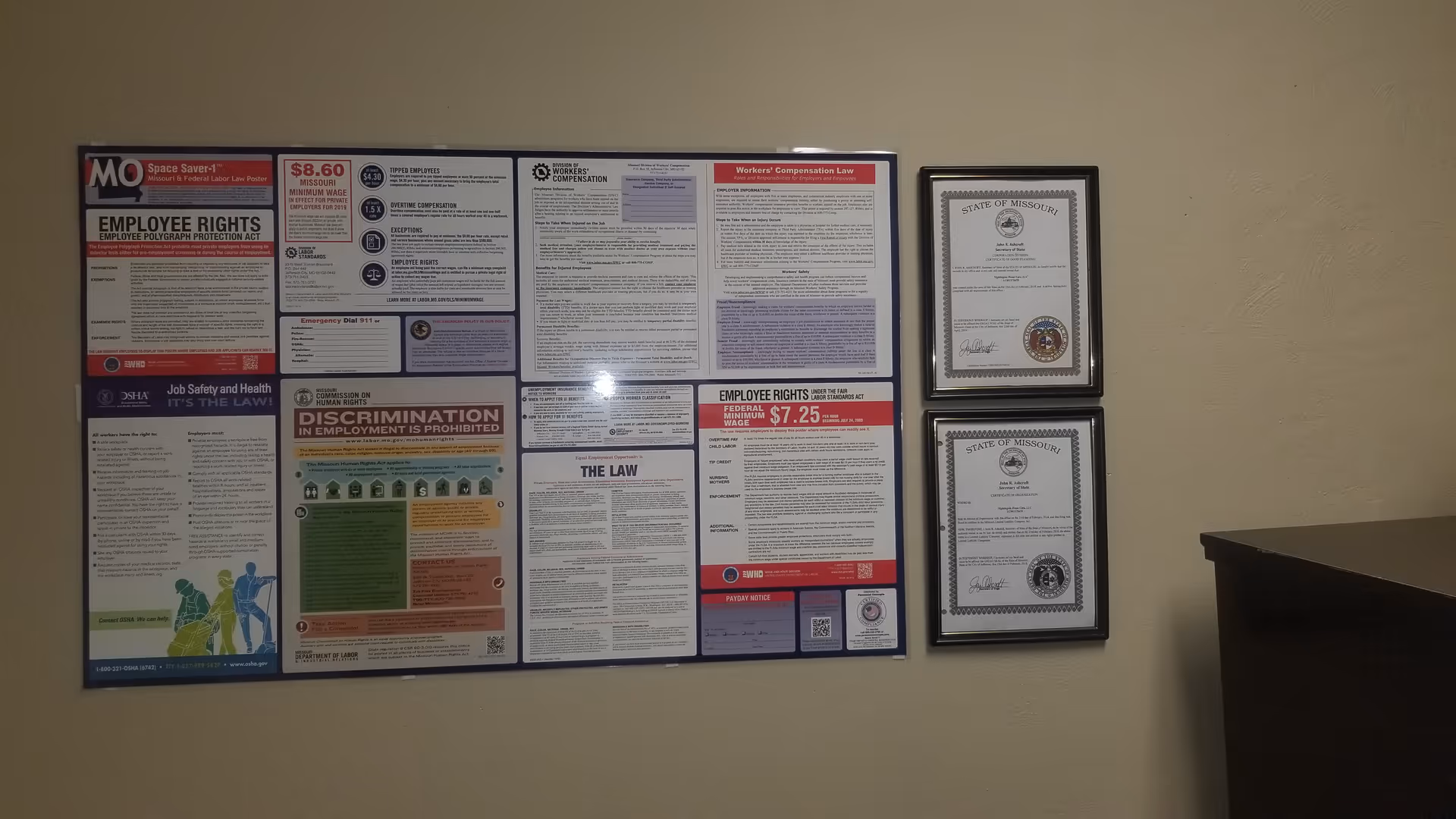 Interior wall with a large bulletin board of employee rights and framed certificates.