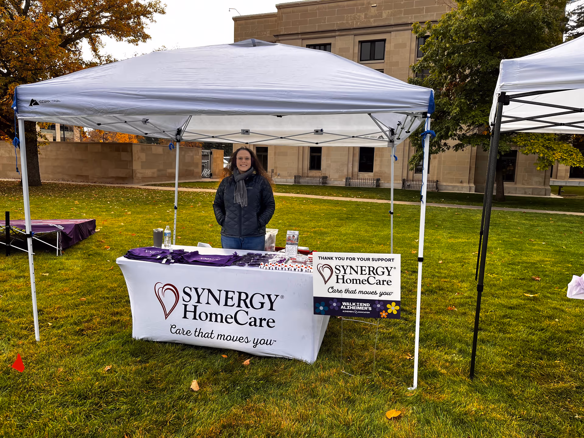 Synergy HomeCare booth under a white canopy on a grassy outdoor lawn.