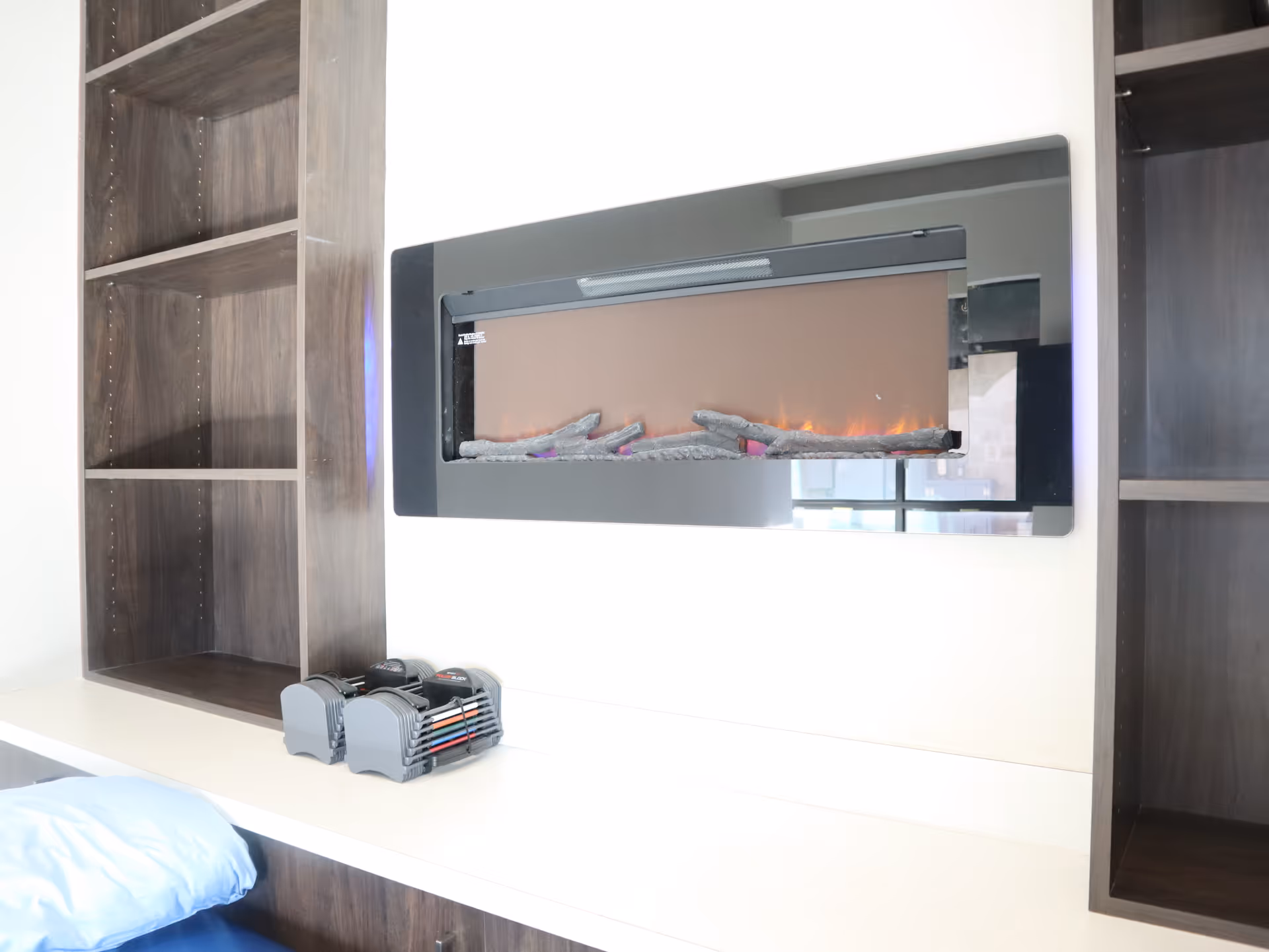 Modern interior featuring a wall-mounted electric fireplace between dark wood shelves and a white counter.