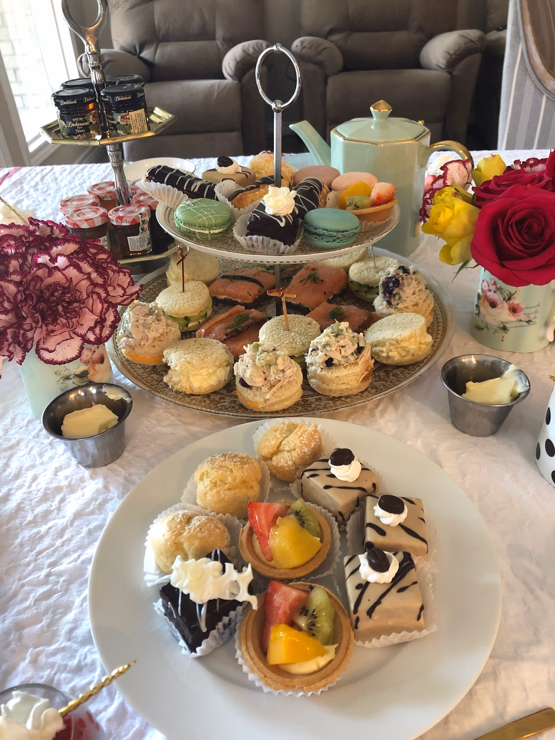 Tiered tray of cupcakes and pastries on a table indoors, with tea and flowers.