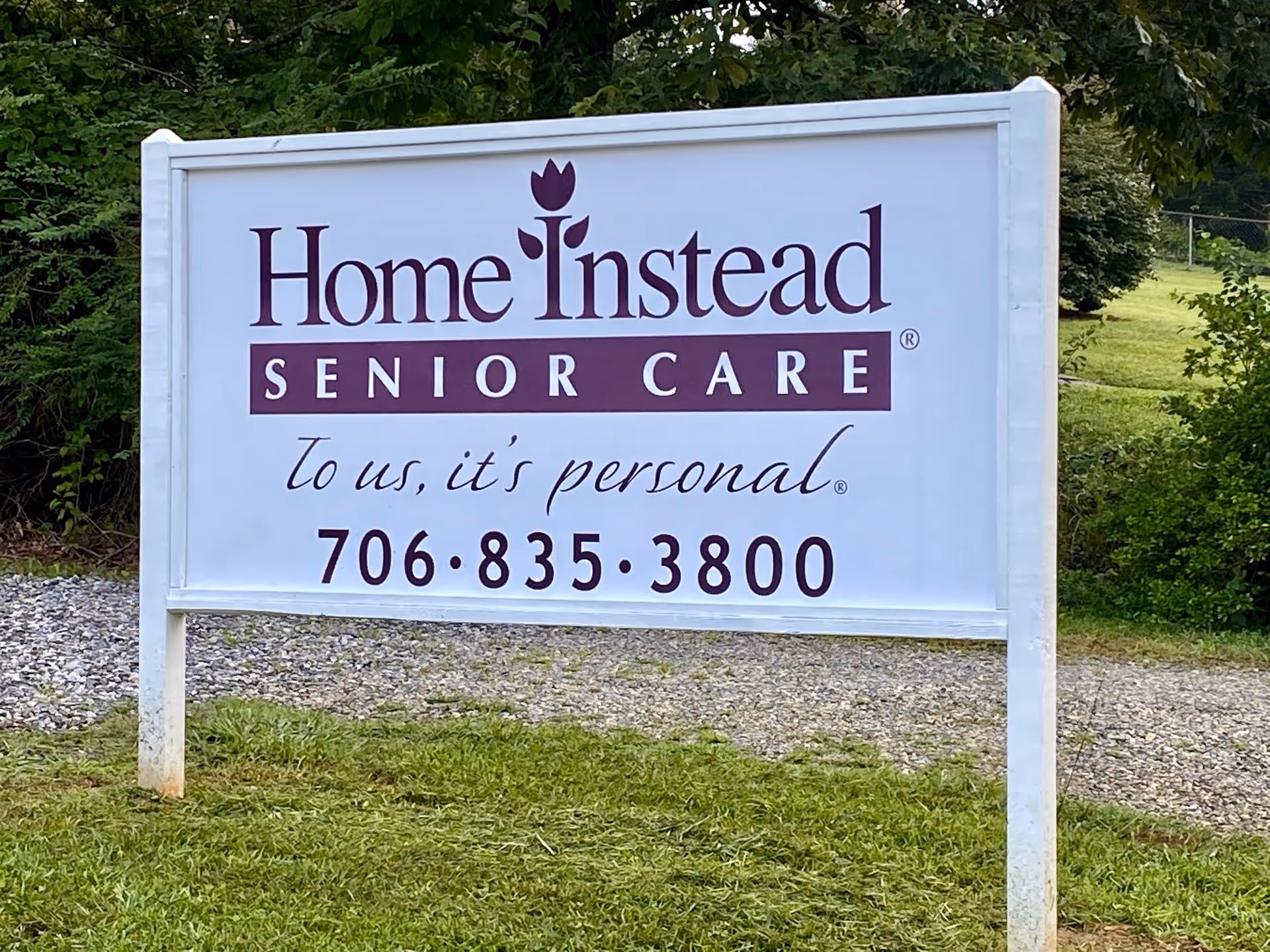 White sign reads Home Instead Senior Care with phone number set on grass.