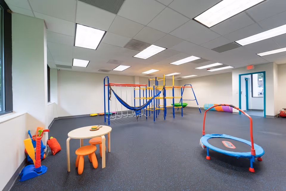 Indoor therapy playroom with colorful climbing structures, a trampoline, and a small activity table.