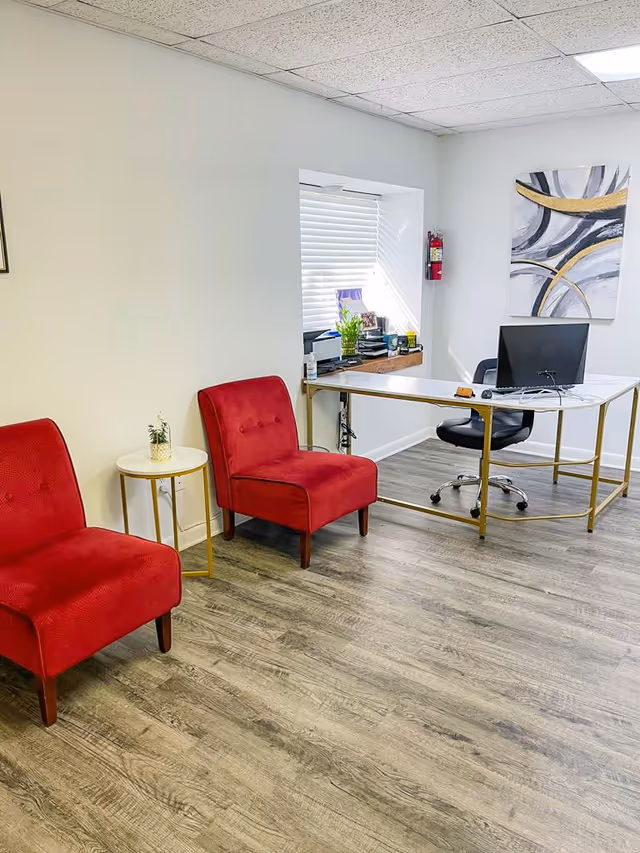 Office reception area with red chairs, a desk, computer, and abstract wall art.