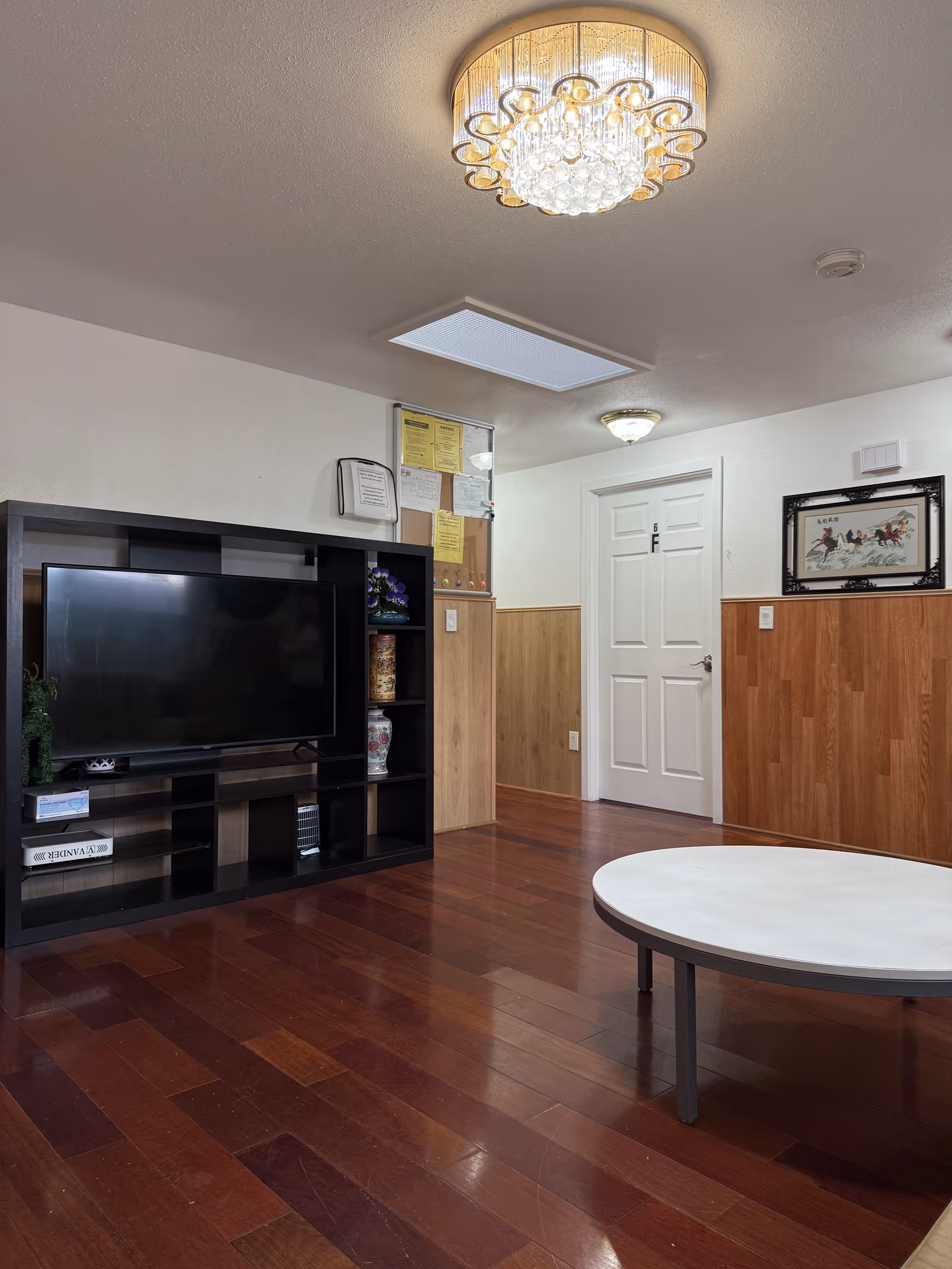 Indoor living area at Anna Adult Family Home with TV, round coffee table, and wood floors.