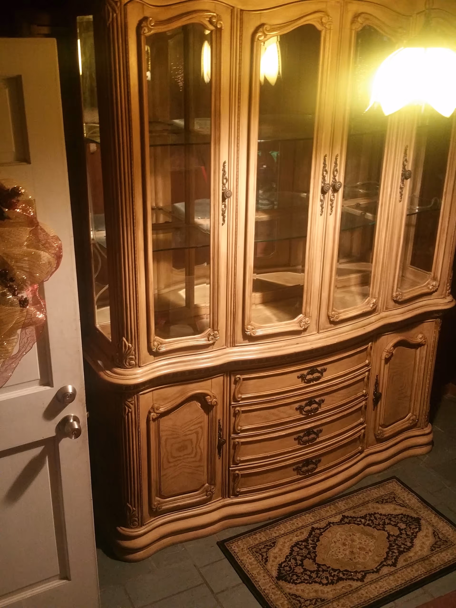 Ornate wooden china cabinet with glass doors stands in a dimly lit interior.