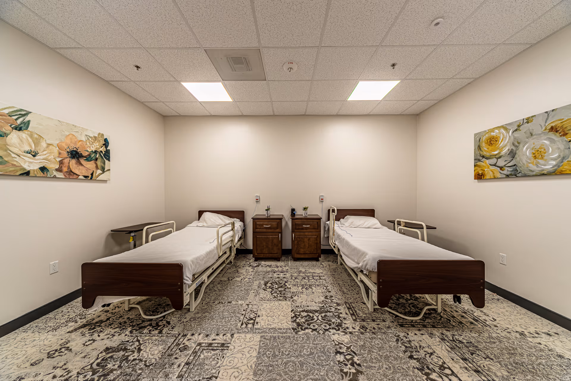 Two wooden hospital beds with white sheets and matching nightstands in a neutral patient room.