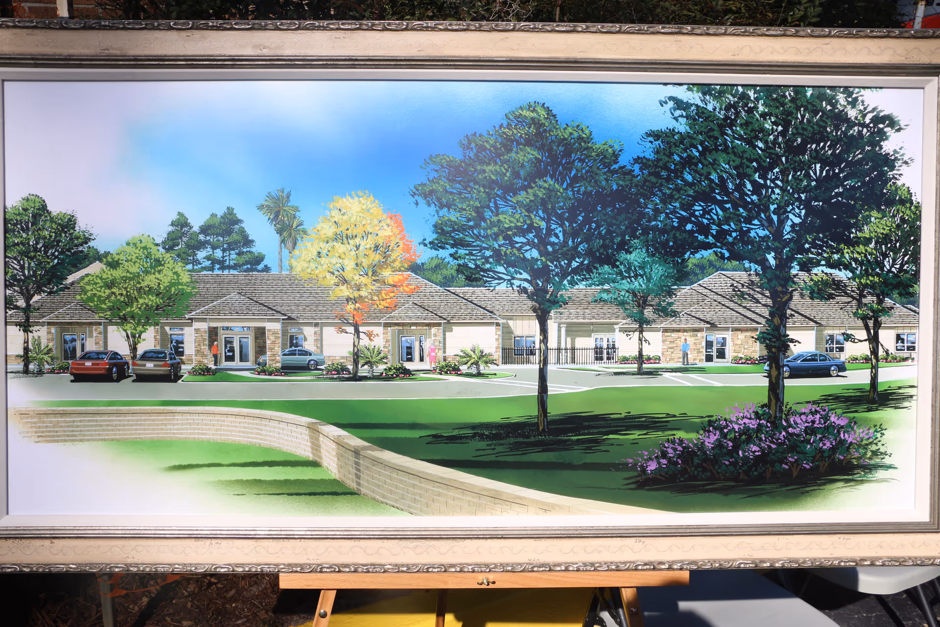 Framed painting of a single-story senior living campus with cars parked and trees.