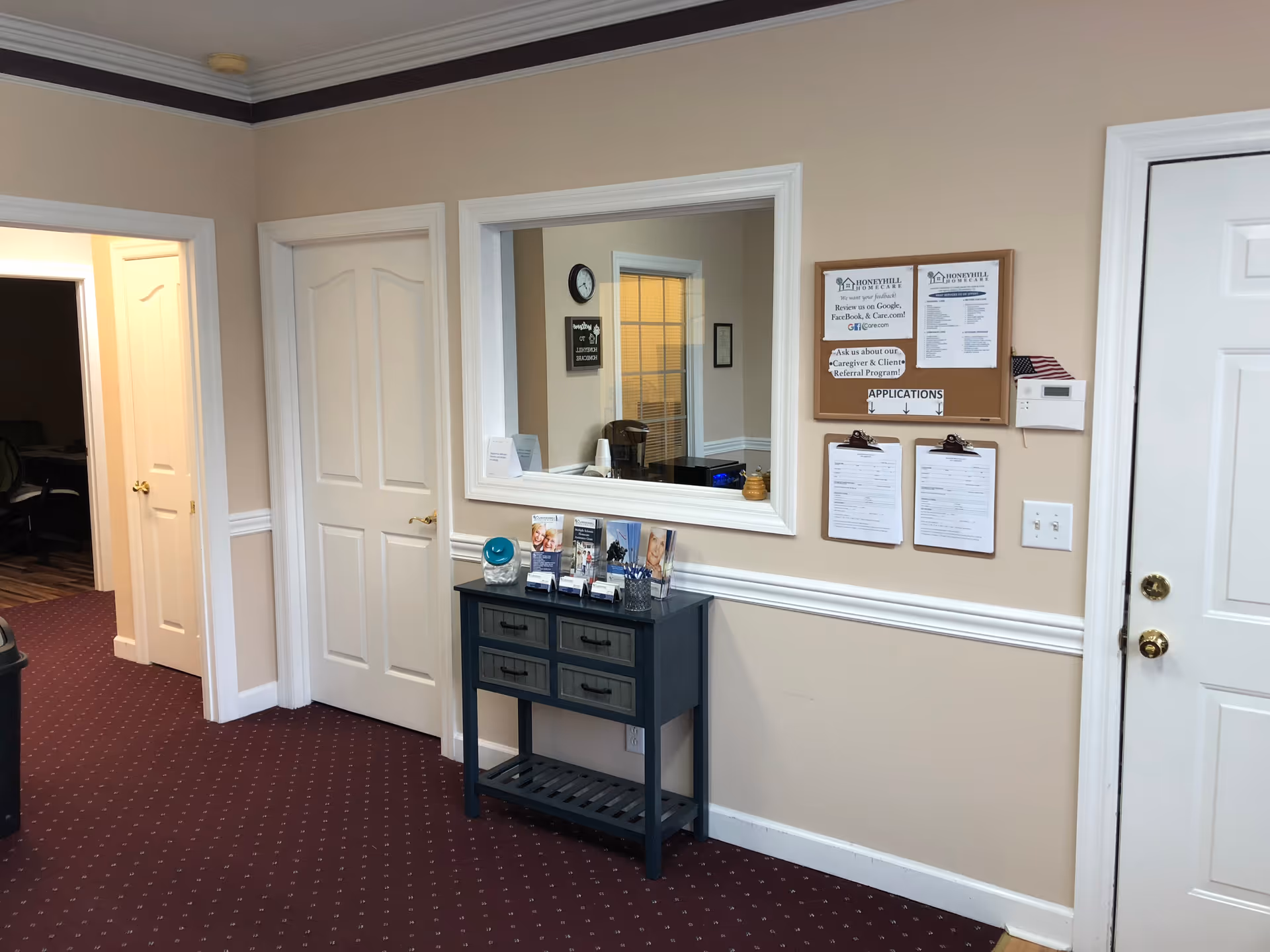 Interior hallway with a reception window, bulletin board, and a dark blue console table near doors.