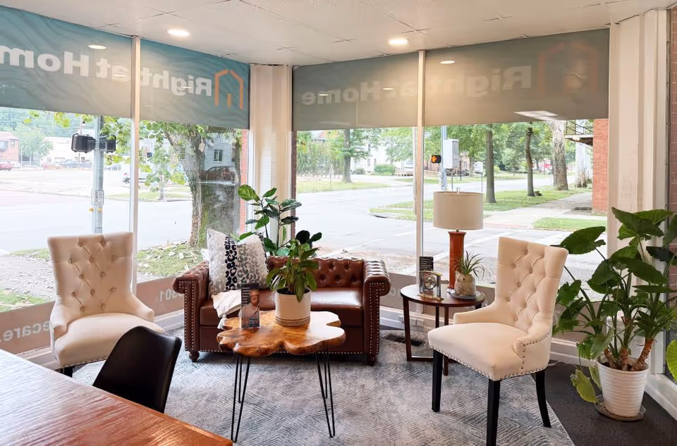 A bright senior living lobby with beige tufted chairs, a brown leather sofa, and plants.