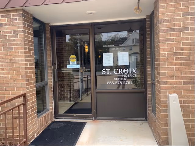 Brick building entrance with glass doors labeled St. Croix Hospice, visible signage and brick exterior.