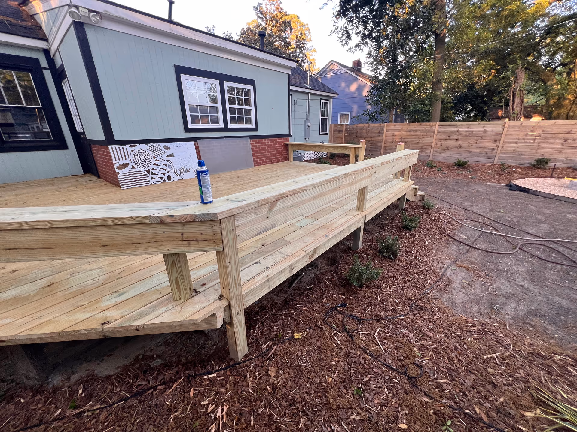 Rough wooden deck under construction attached to blue house with a water bottle on the railing.