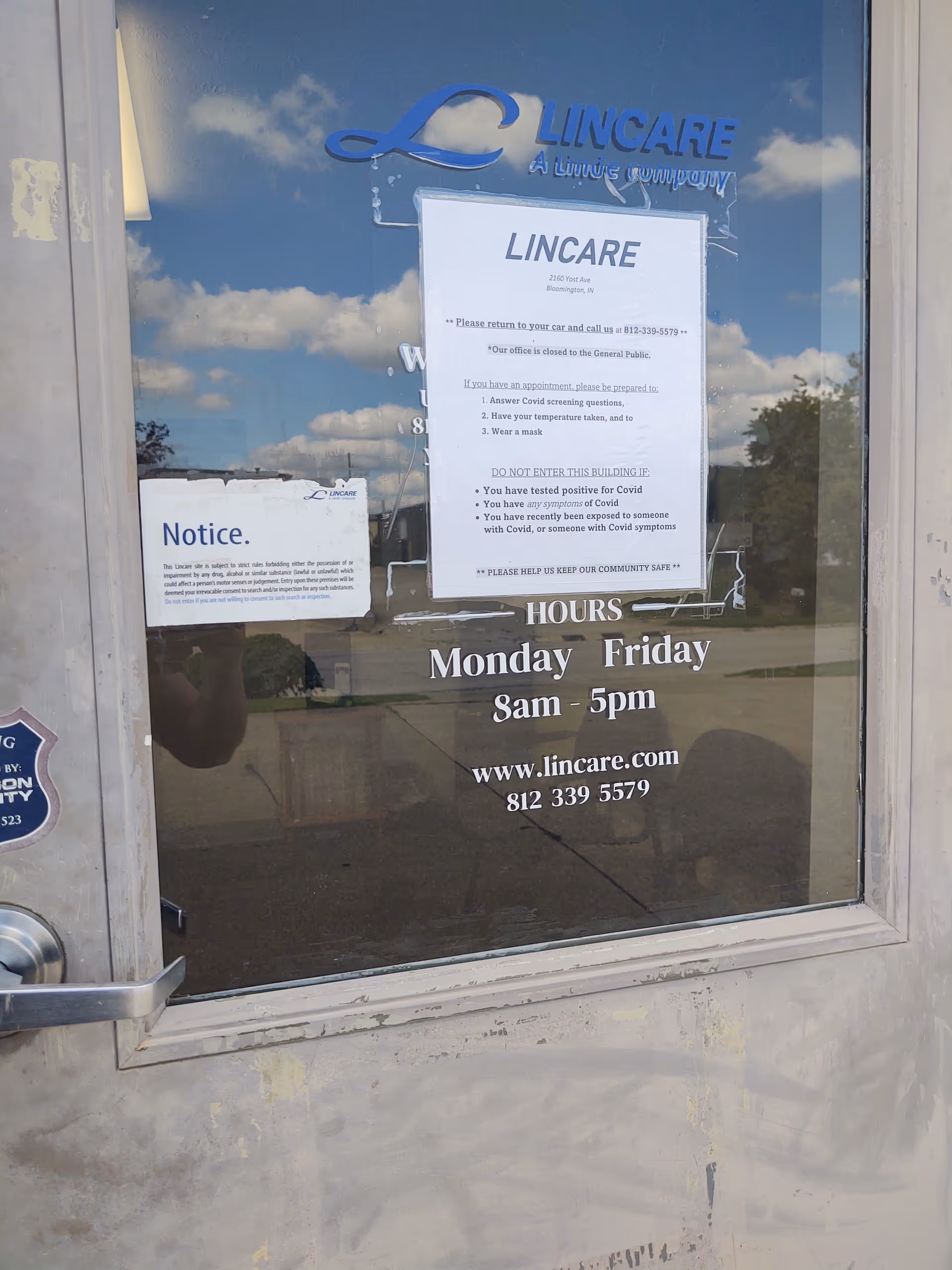 Exterior glass door of LINCARE facility with posted notices, hours, and contact information.
