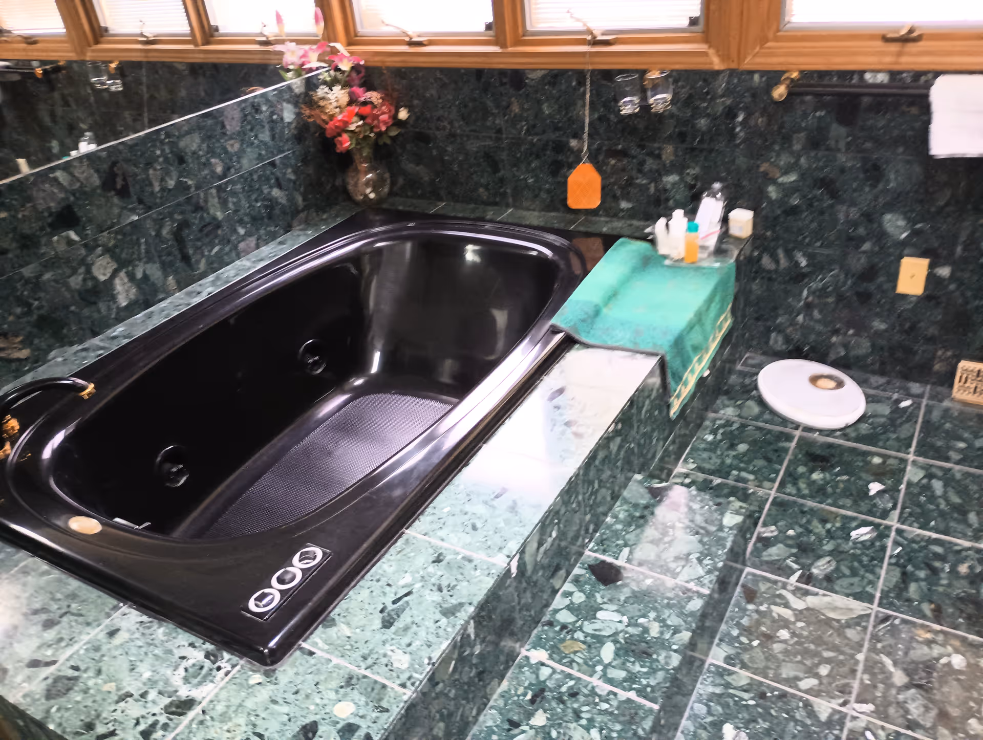 Green marble bathroom with a black soaking tub and toiletries on the counter