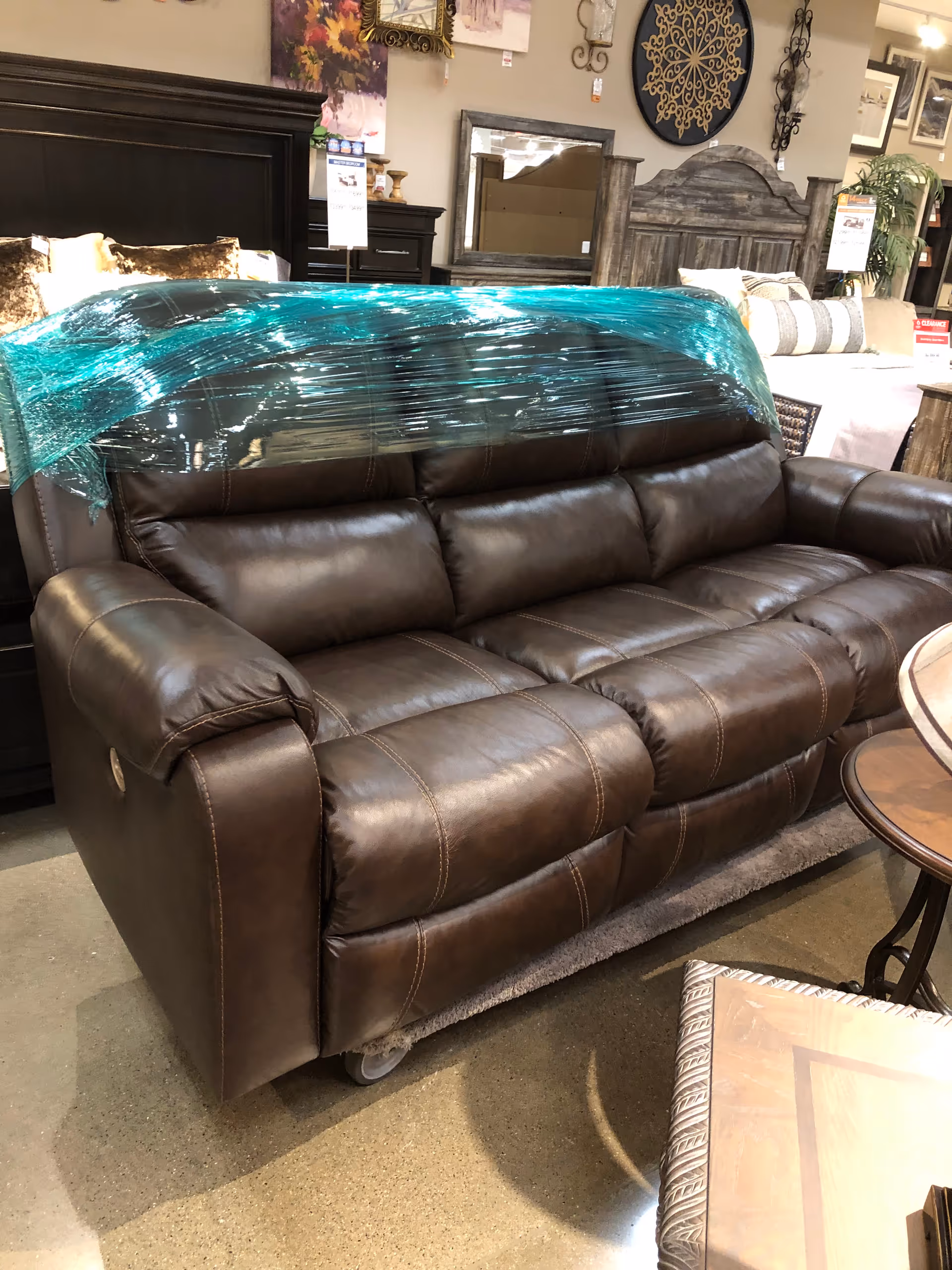 Brown leather sofa in a furniture showroom with teal plastic wrap on the back