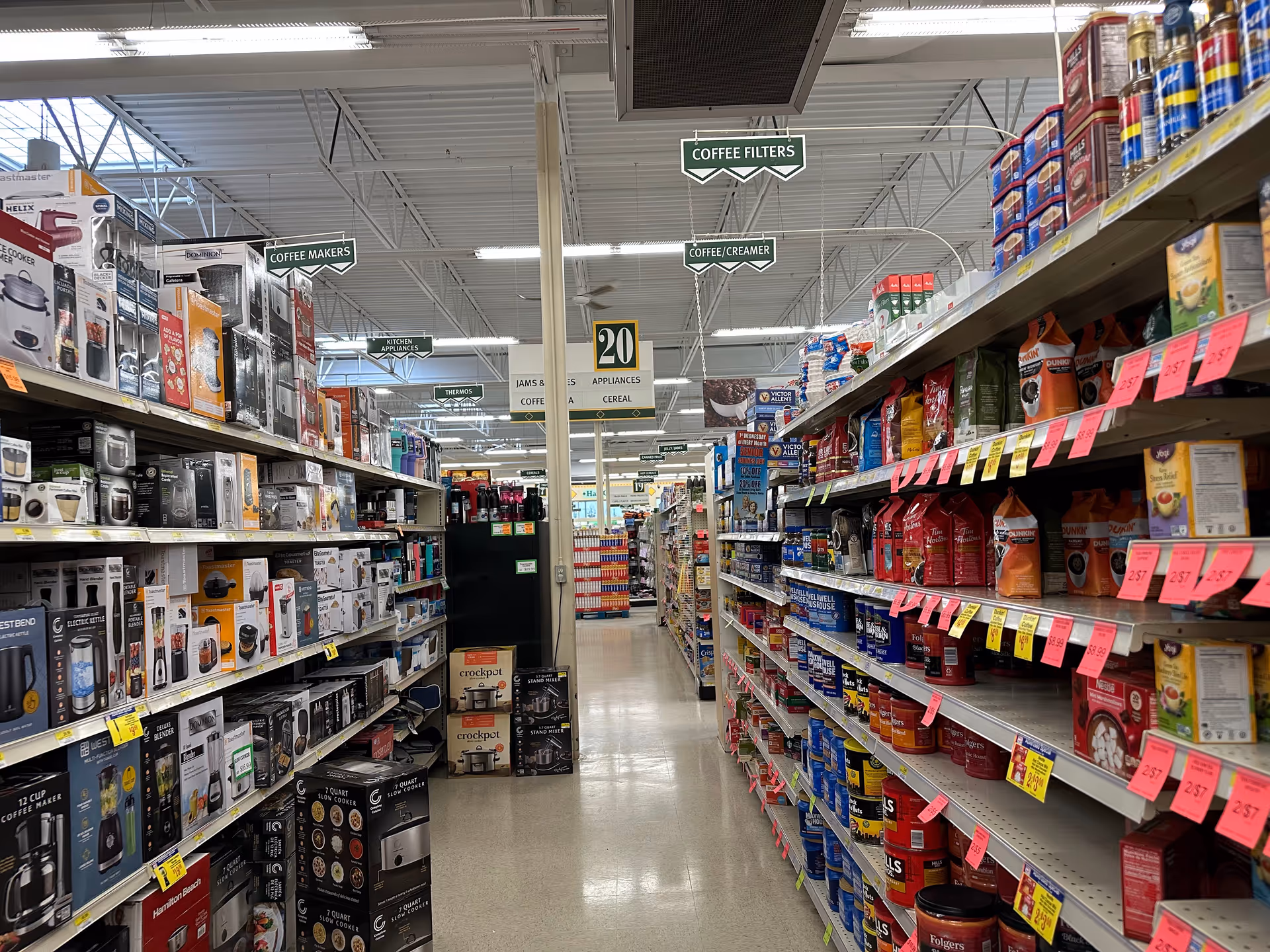 Well-lit store aisle with shelves of coffee makers and pantry items.